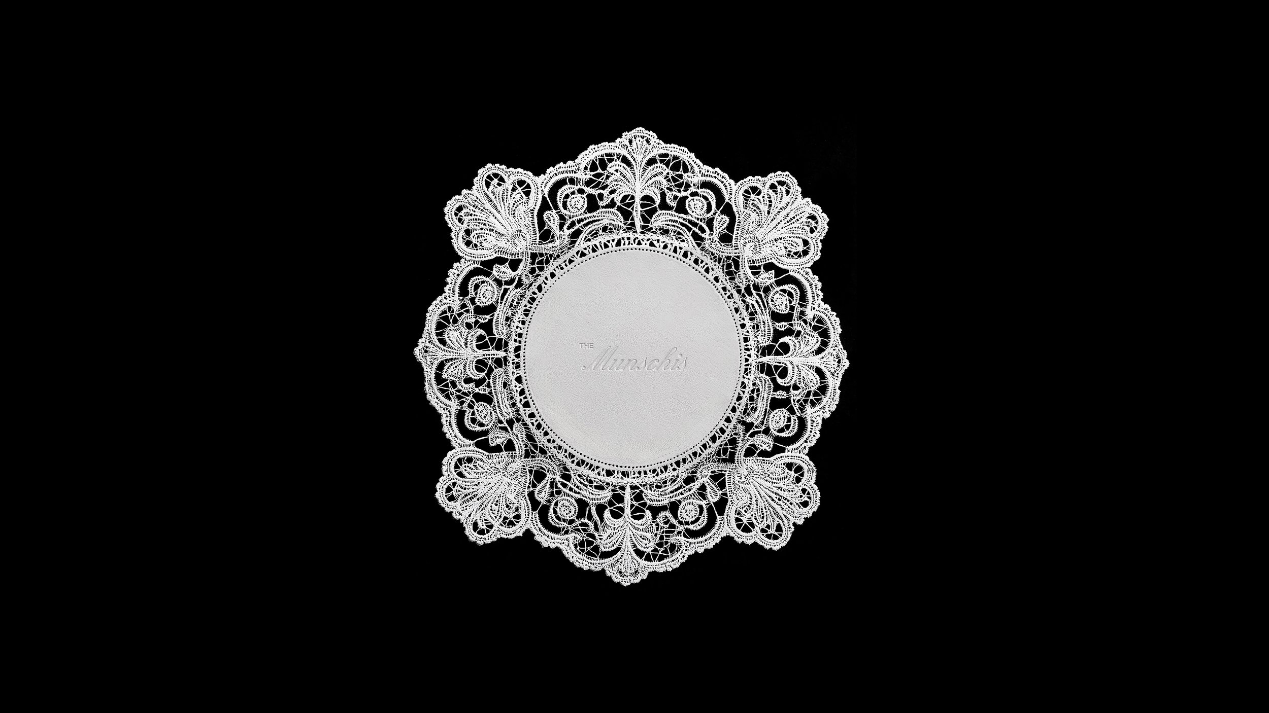 A round lace doily with intricate floral patterns surrounds a circular piece of paper.