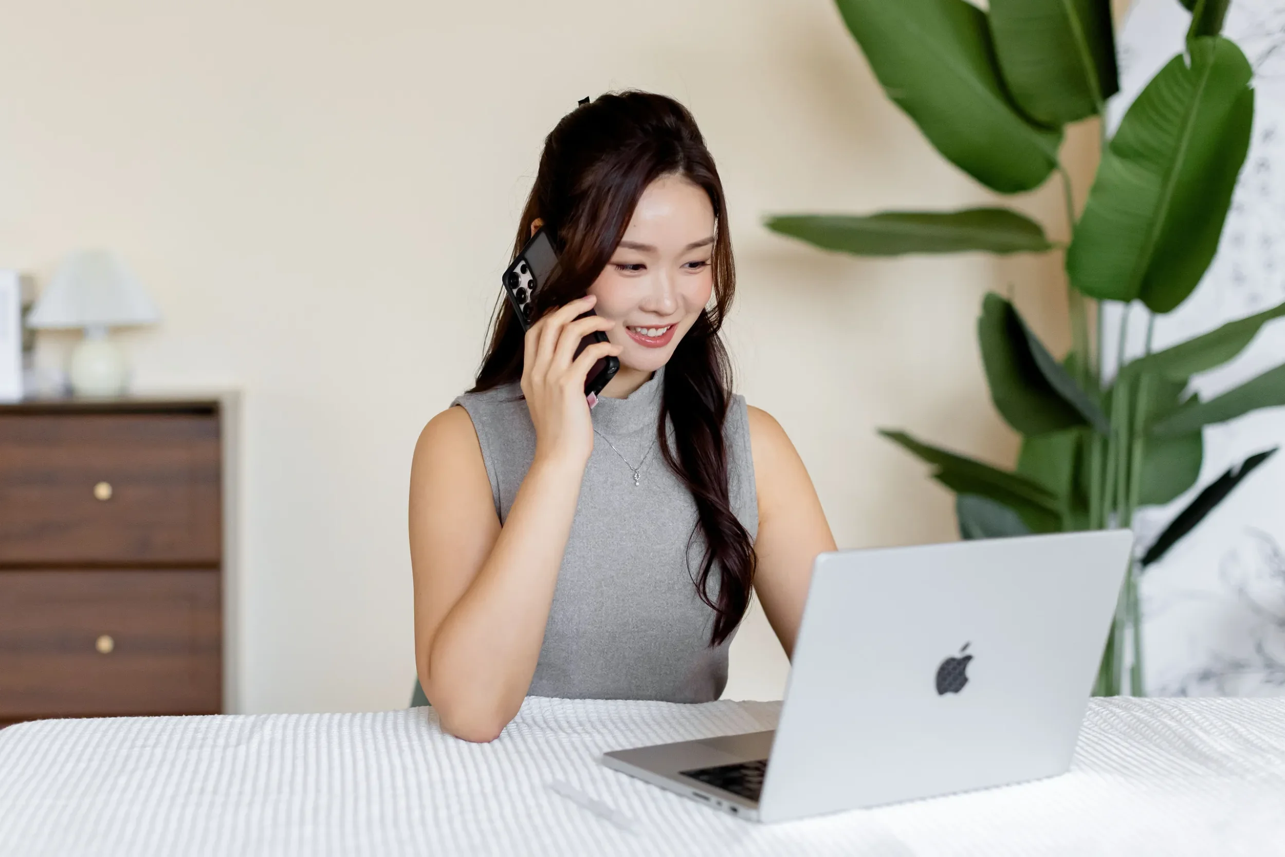 Adrienna Siew, Singapore property advisor focused on new launch condos, seated at a table with an open laptop while speaking on her phone.