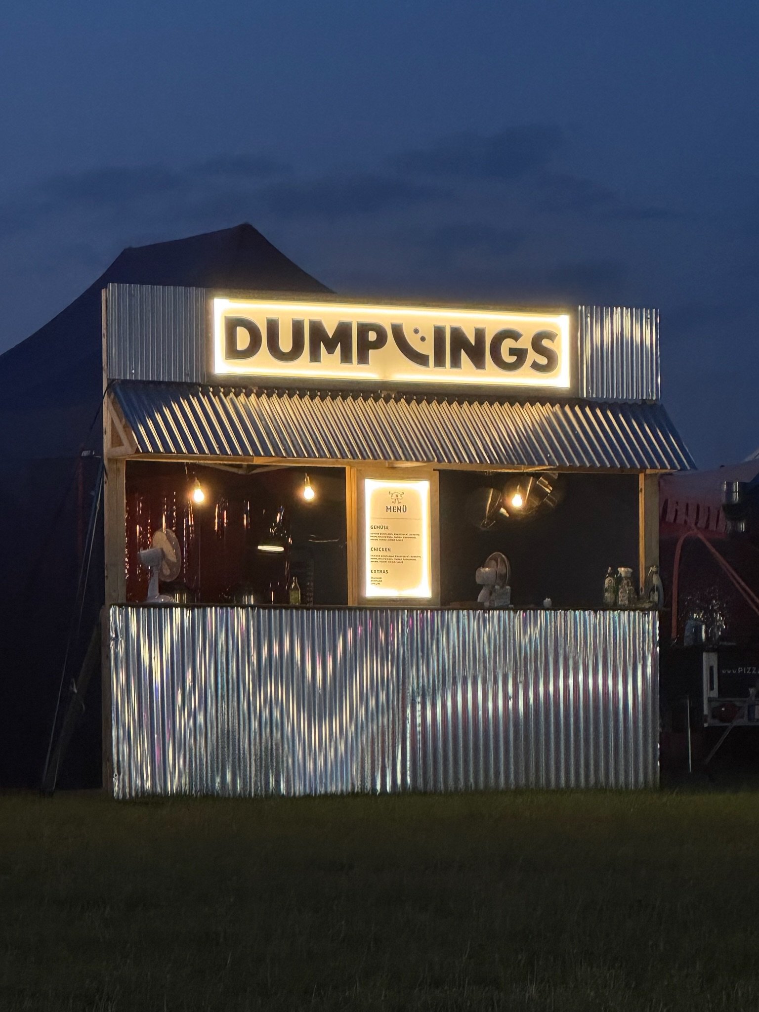 Abdeckung eines Imbisswagens mit einem leuchtenden Schild, auf dem 'DUMPINGS' steht, bei Nacht.