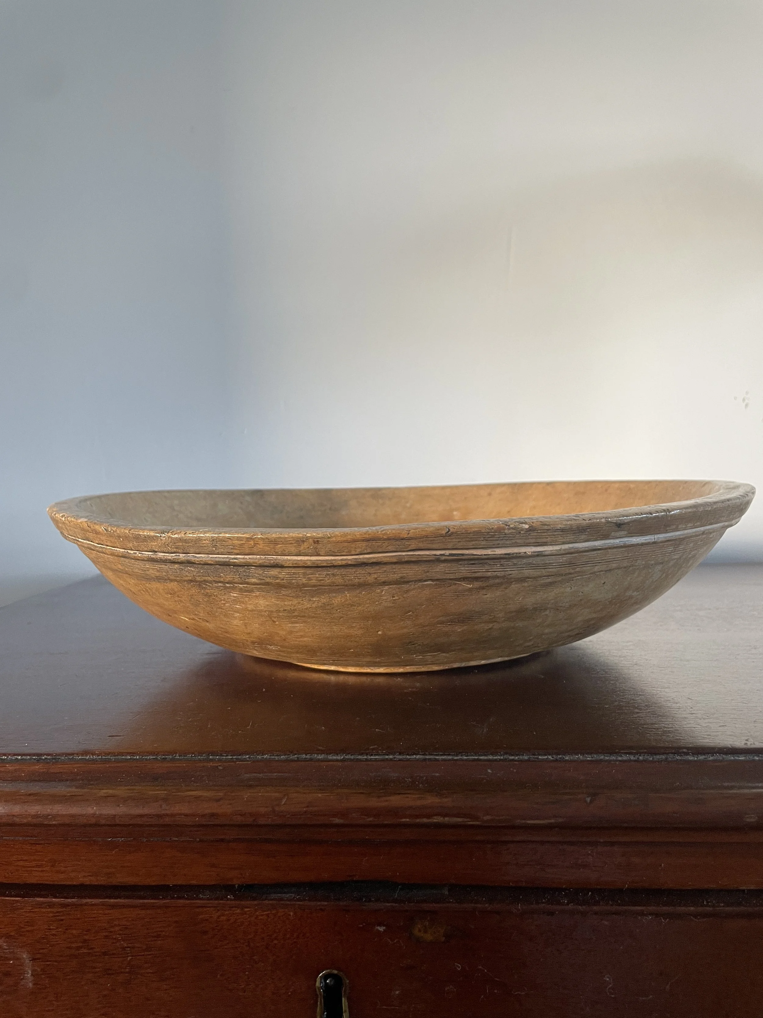 An empty wooden bowl sitting on a dark wooden surface with a light-colored background.