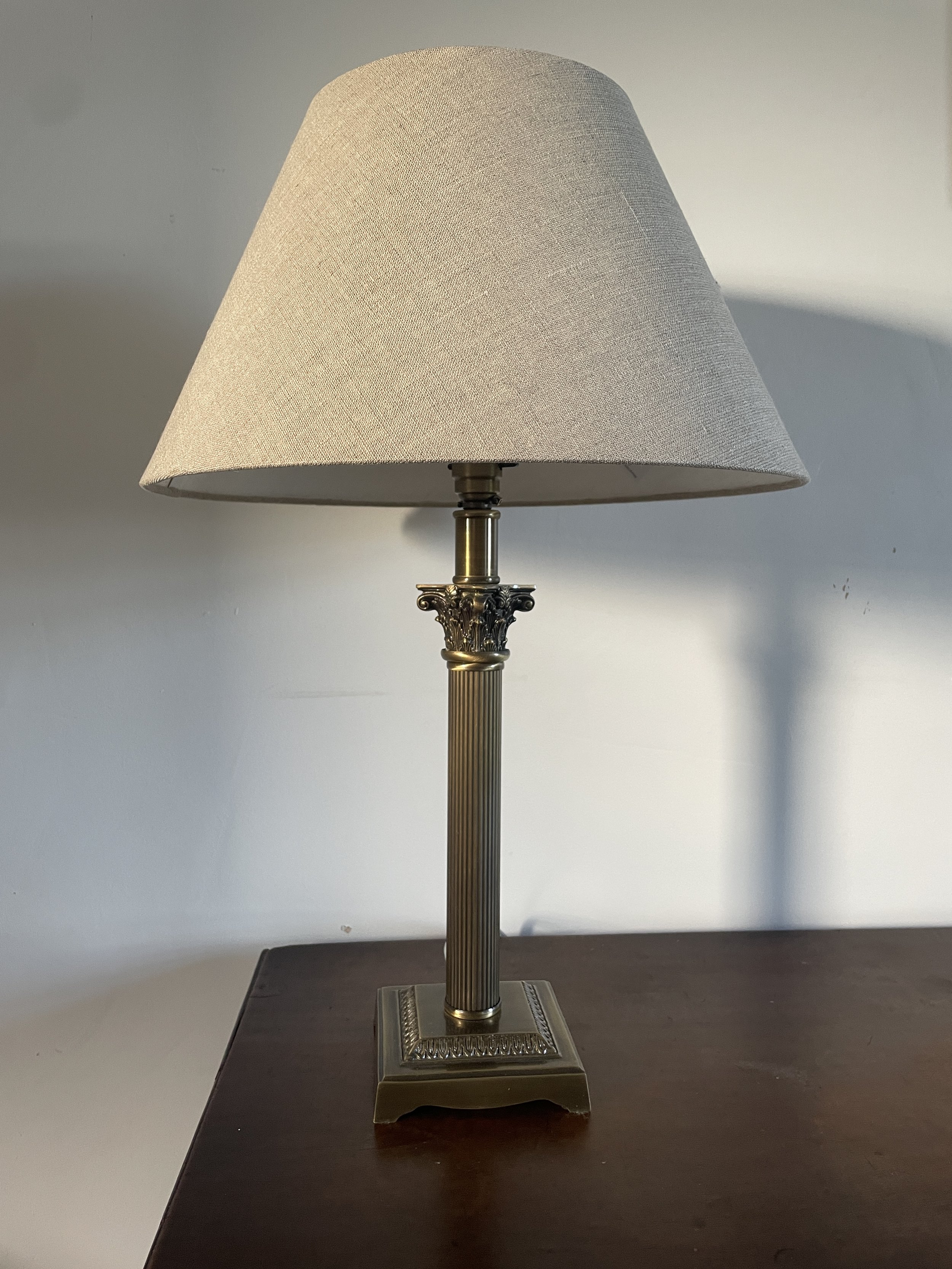 A table lamp with a beige fabric lampshade and ornate metallic base on a dark wooden surface.