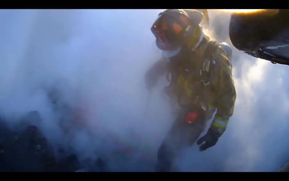 Firefighter in protective gear and helmet working in smoke or fog.