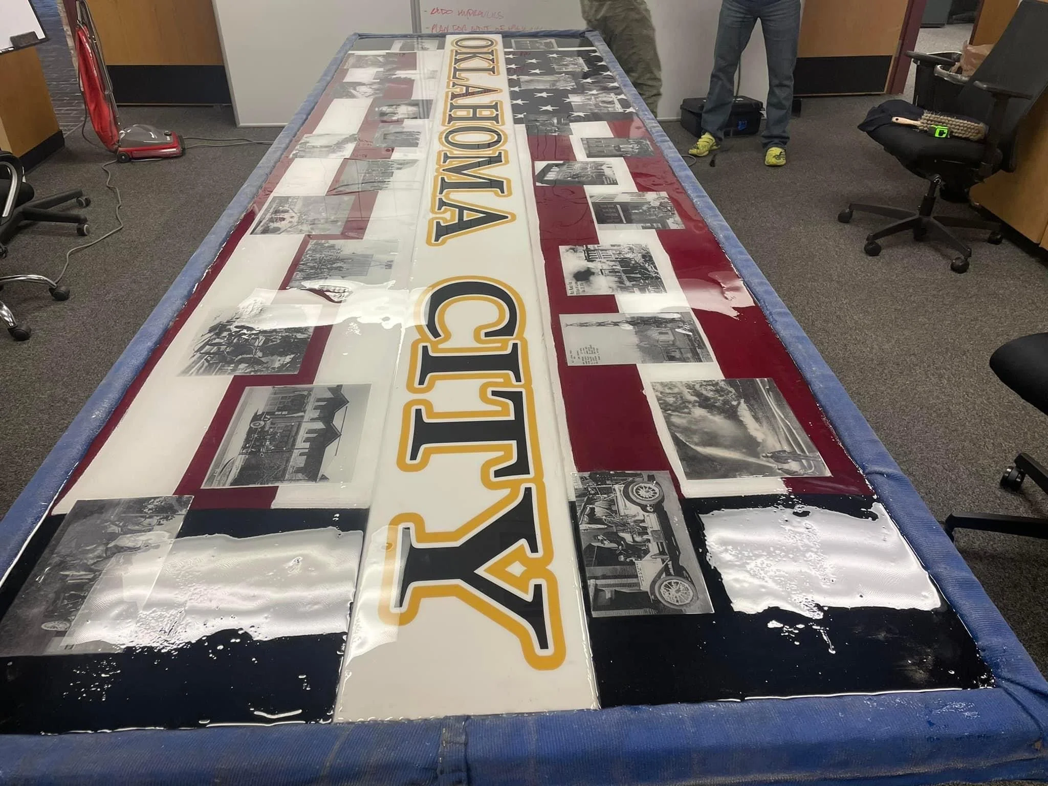 Long table with a sign that reads 'OKLAHOMA CITY' and black-and-white photographs. The table is has old fire department pictures, challenge coins, american flag, set on fire hydrants.