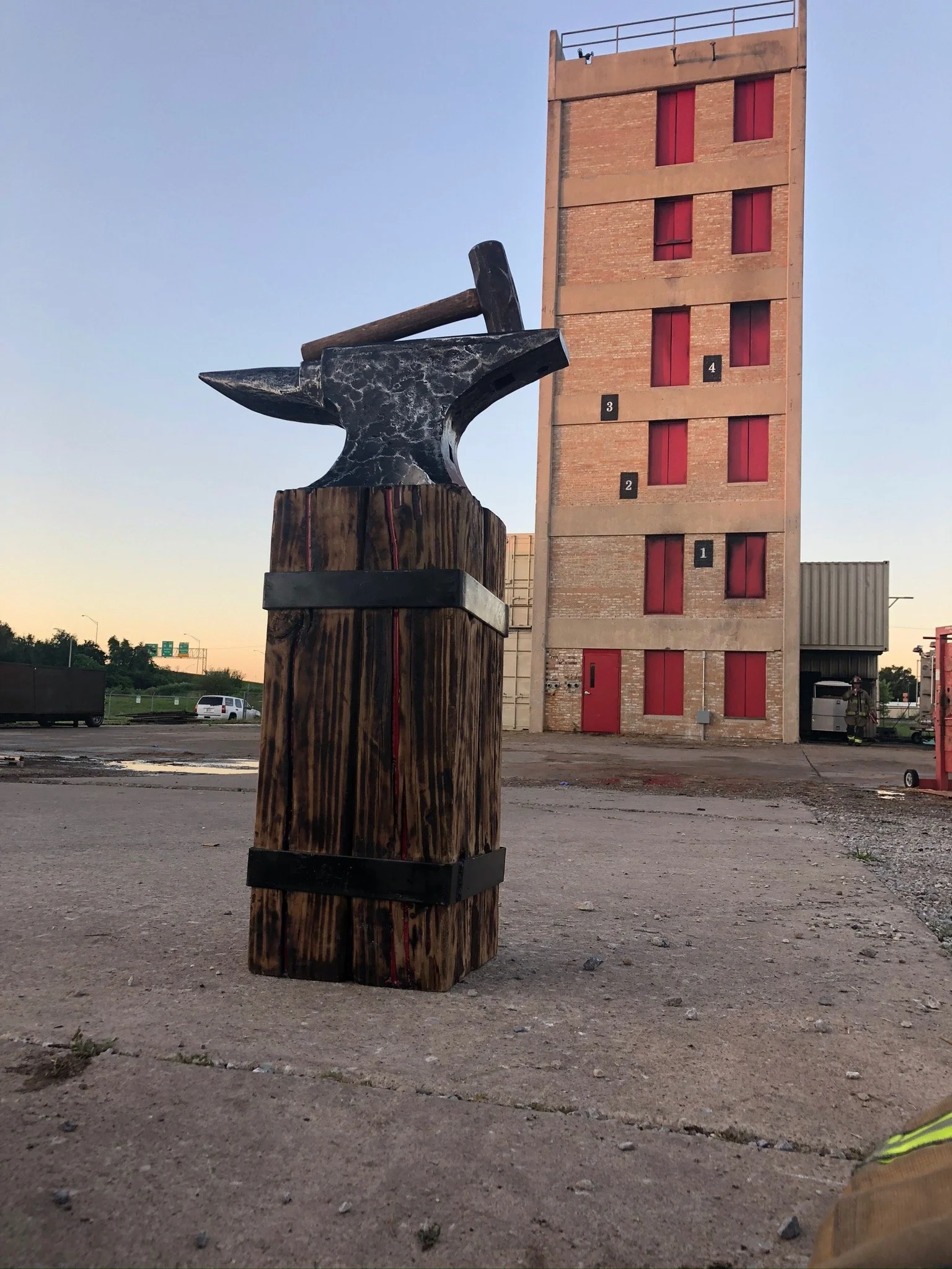 A sculpture of an anvil with a hammer resting on it, mounted on a wooden pedestal, Fire department symbol