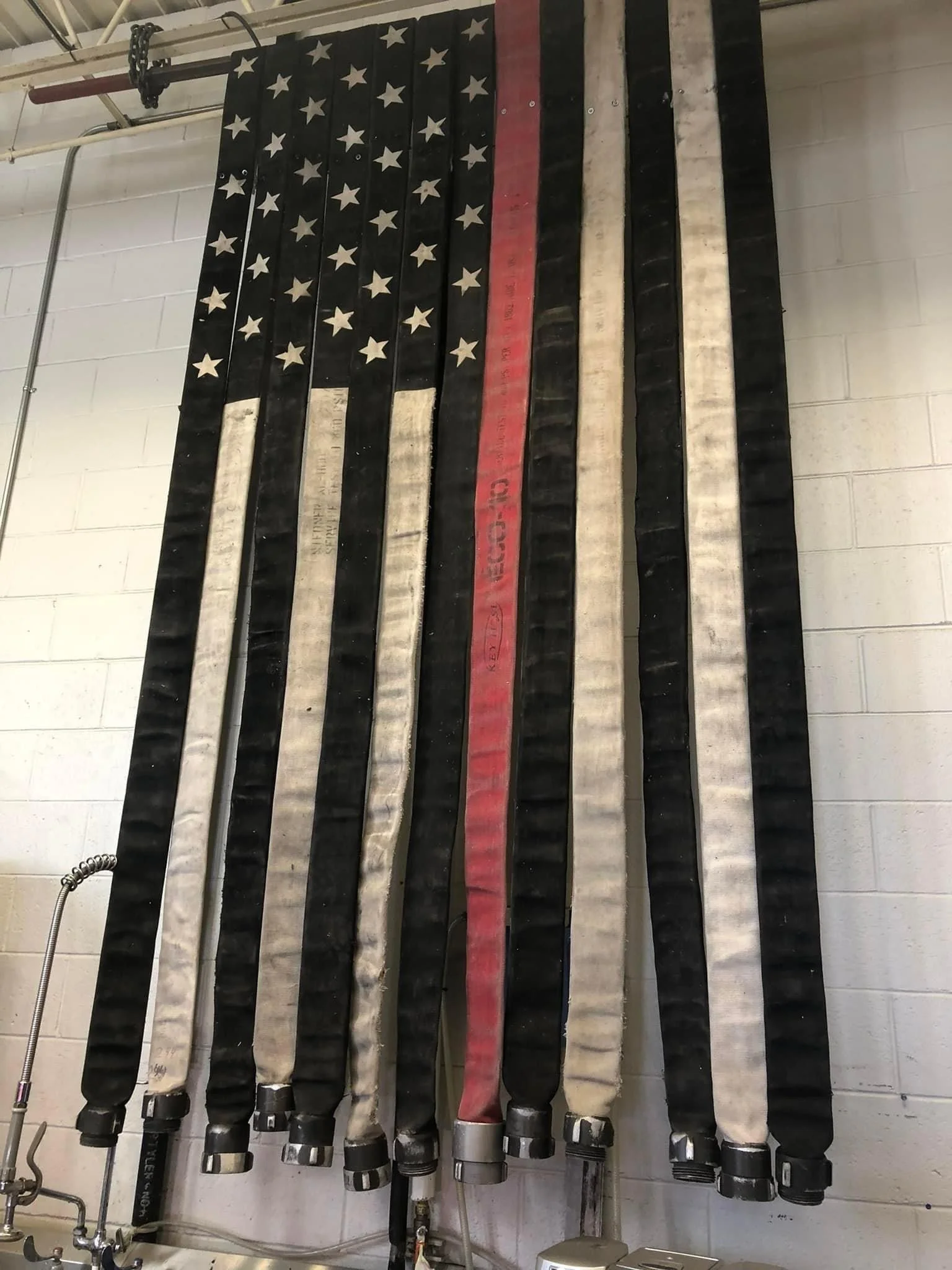 A large American flag made from firefighting hoses hanging on a wall.