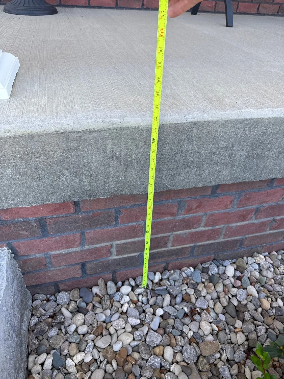 Measuring the height of a brick step with a yellow tape measure. The tape shows approximately 7 inches.