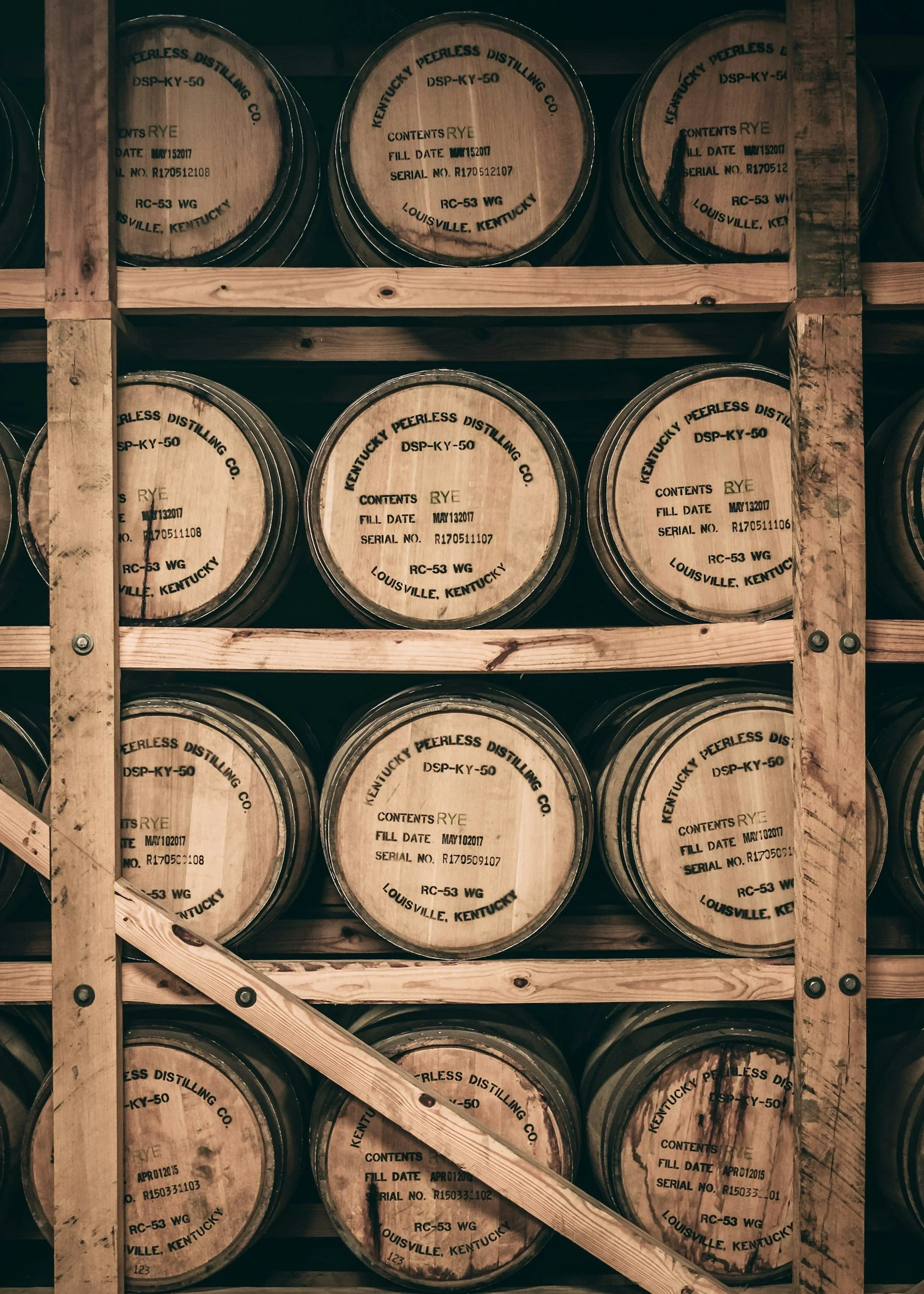 Stacks of wooden barrels labeled with distillery information, stored on wooden shelves in a warehouse.