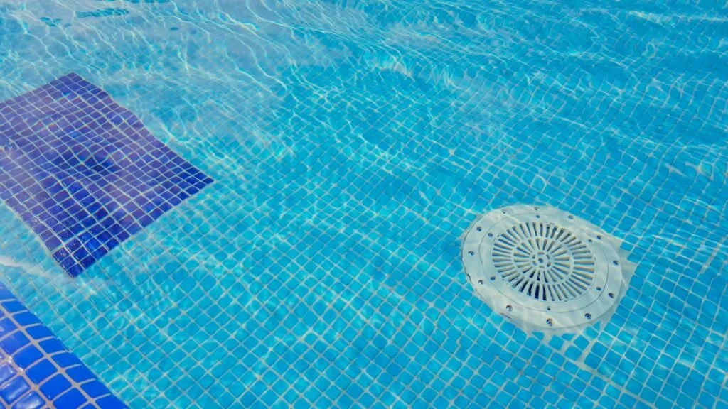Close-up of a swimming pool with blue tiles, a pool drain, and a dark blue tiled step.