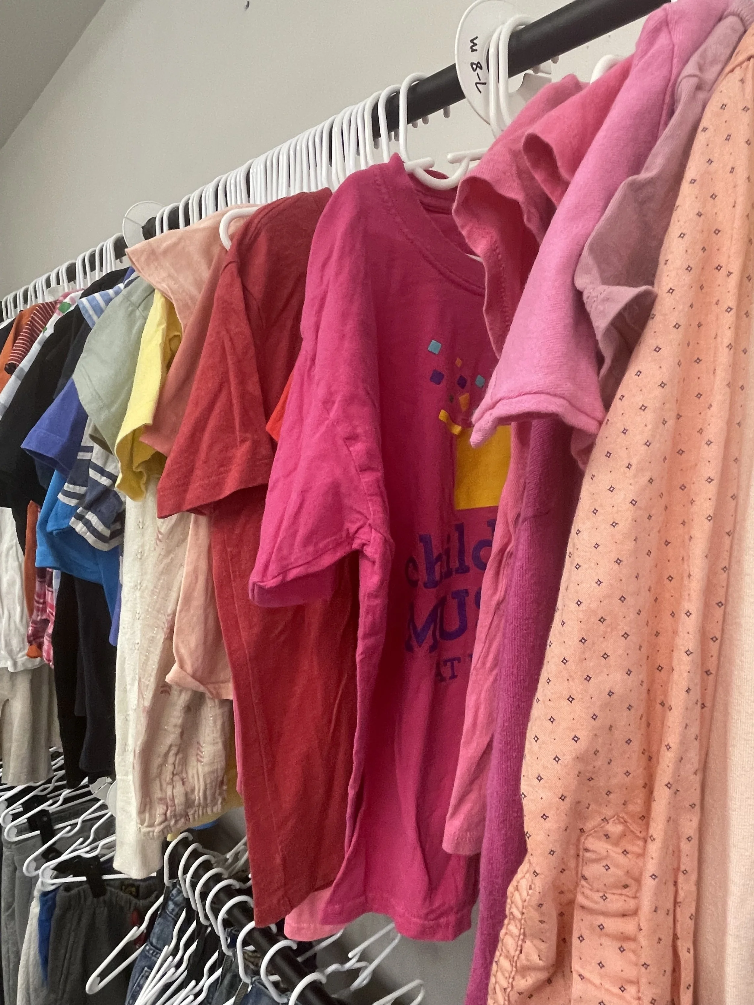 Clothes hanging on a rack, including t-shirts and pajamas in various colors like pink, red, yellow, and blue.
