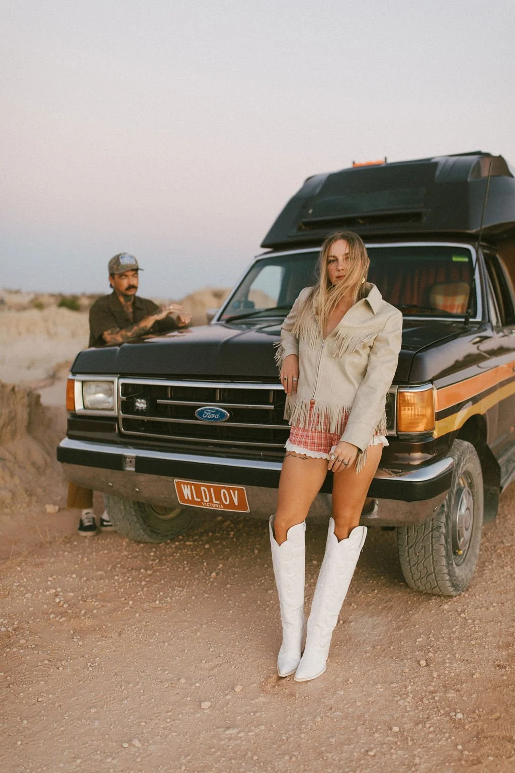 Couple leaning on their old Ford car turned caravan in a creative couples photoshoot, by Kacie Herd.