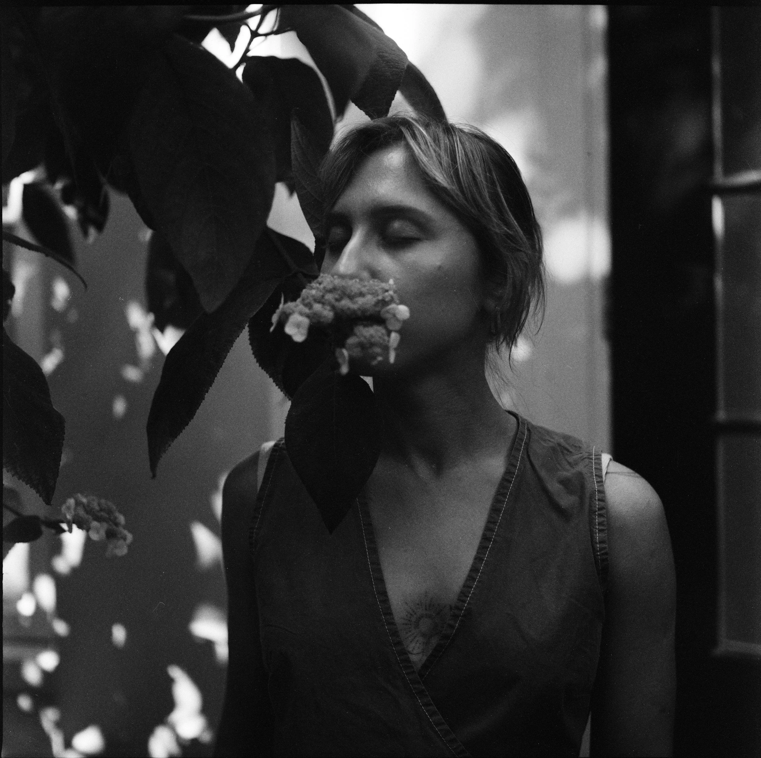 Une femme avec des cheveux courts, les yeux fermés, à côté de feuilles et de fleurs, en noir et blanc.