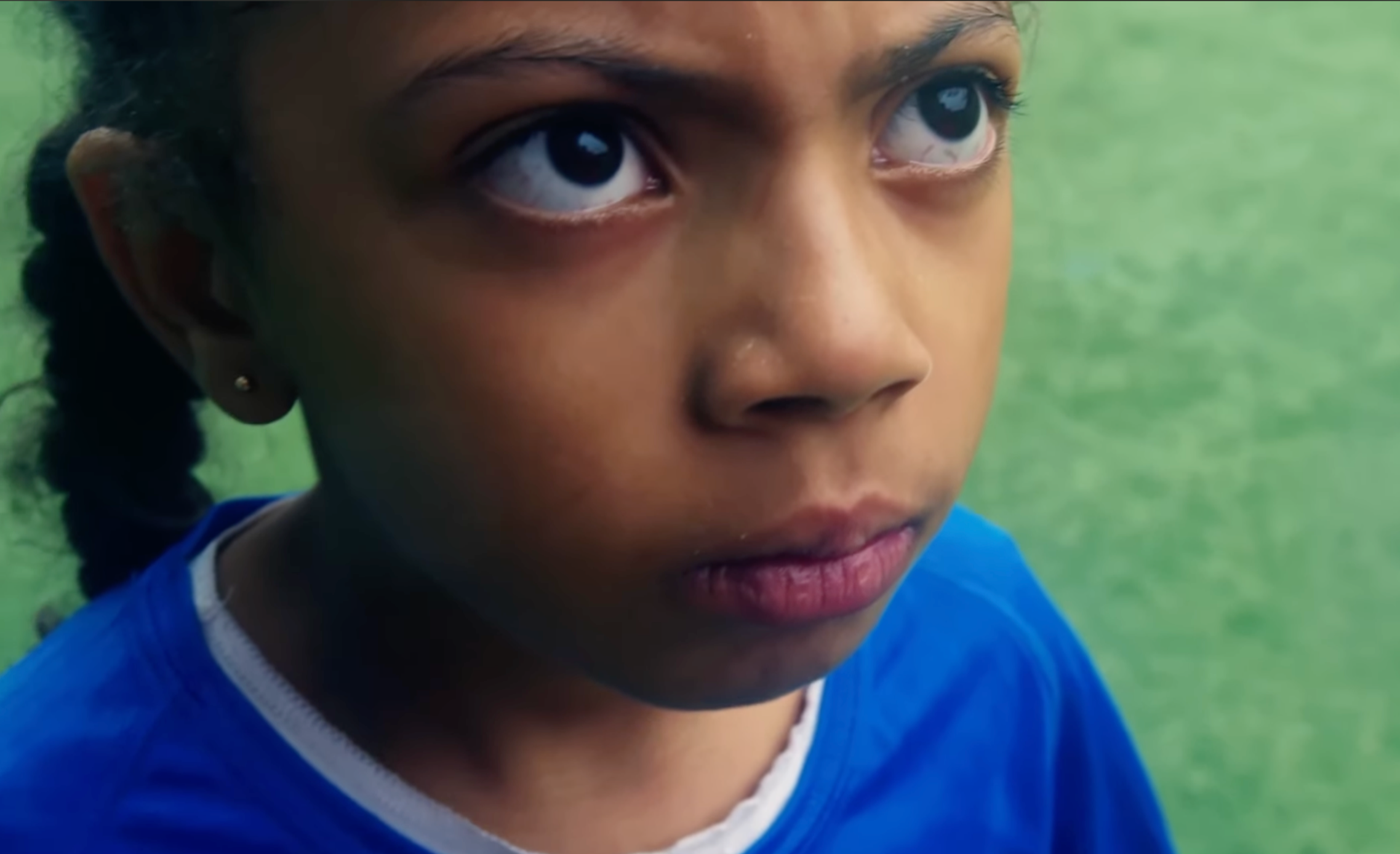 Jeune fille regardant pensivement, de près, avec un fond vert flou.