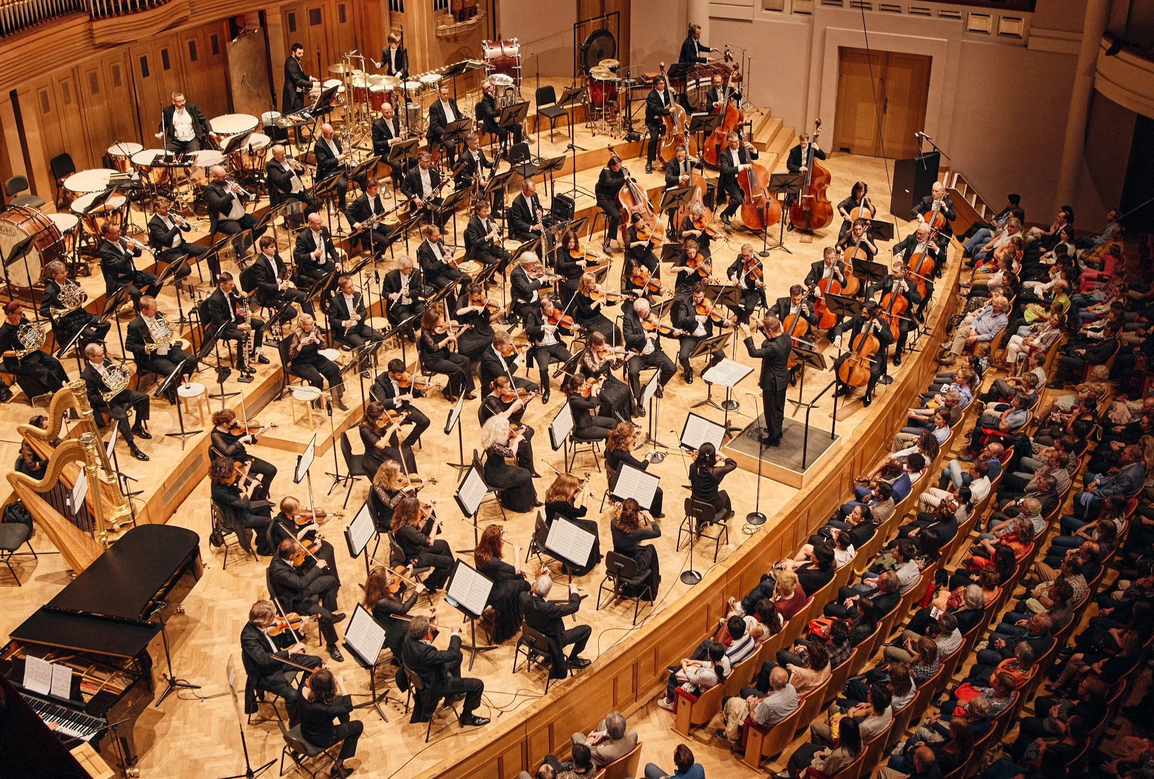 Orkestermuziekoptreden in concertzaal met dirigent, orkestleden en publiek.
