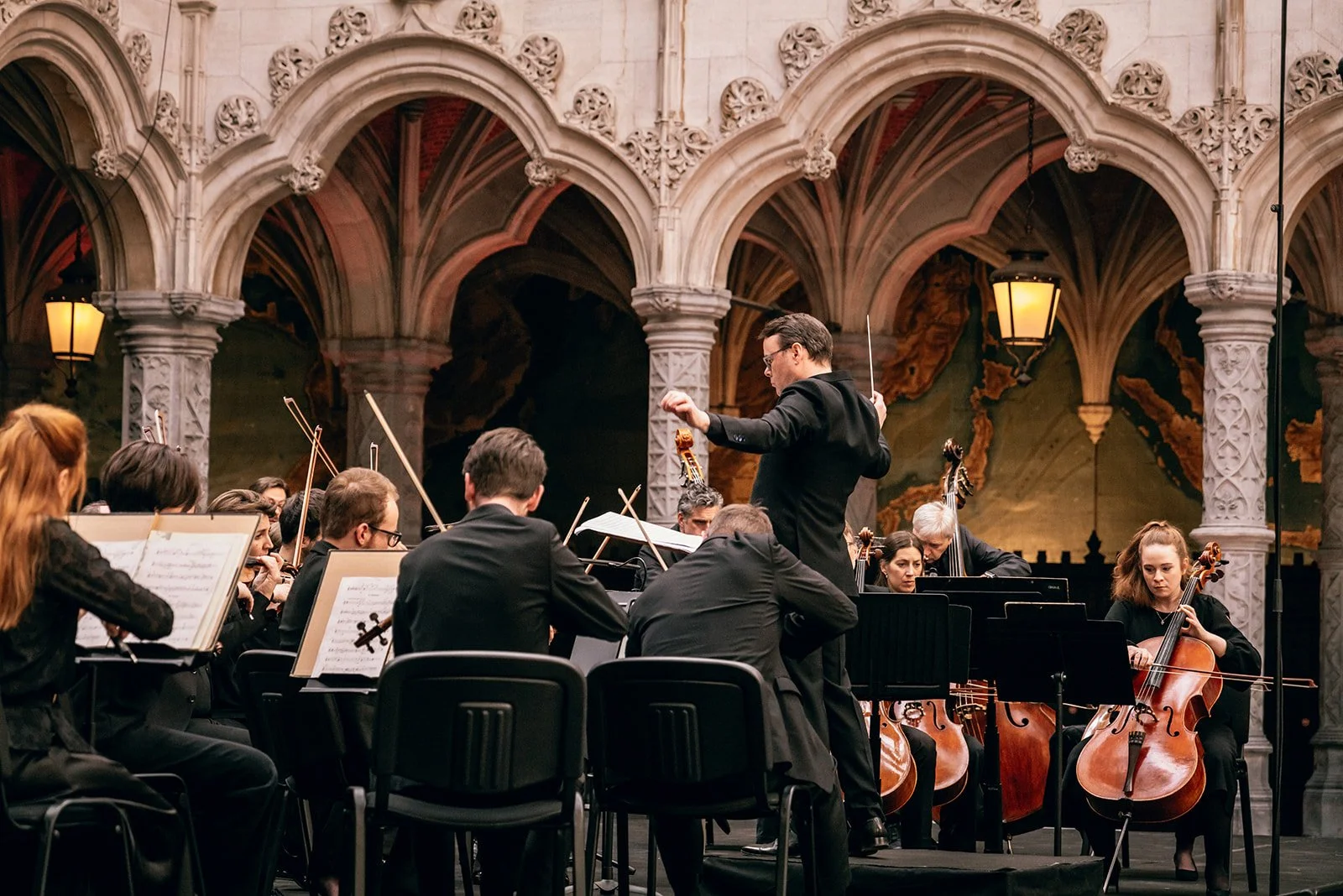 Orkestmusici in een concertzaal die een dirigent volgen, met violen en cello's.