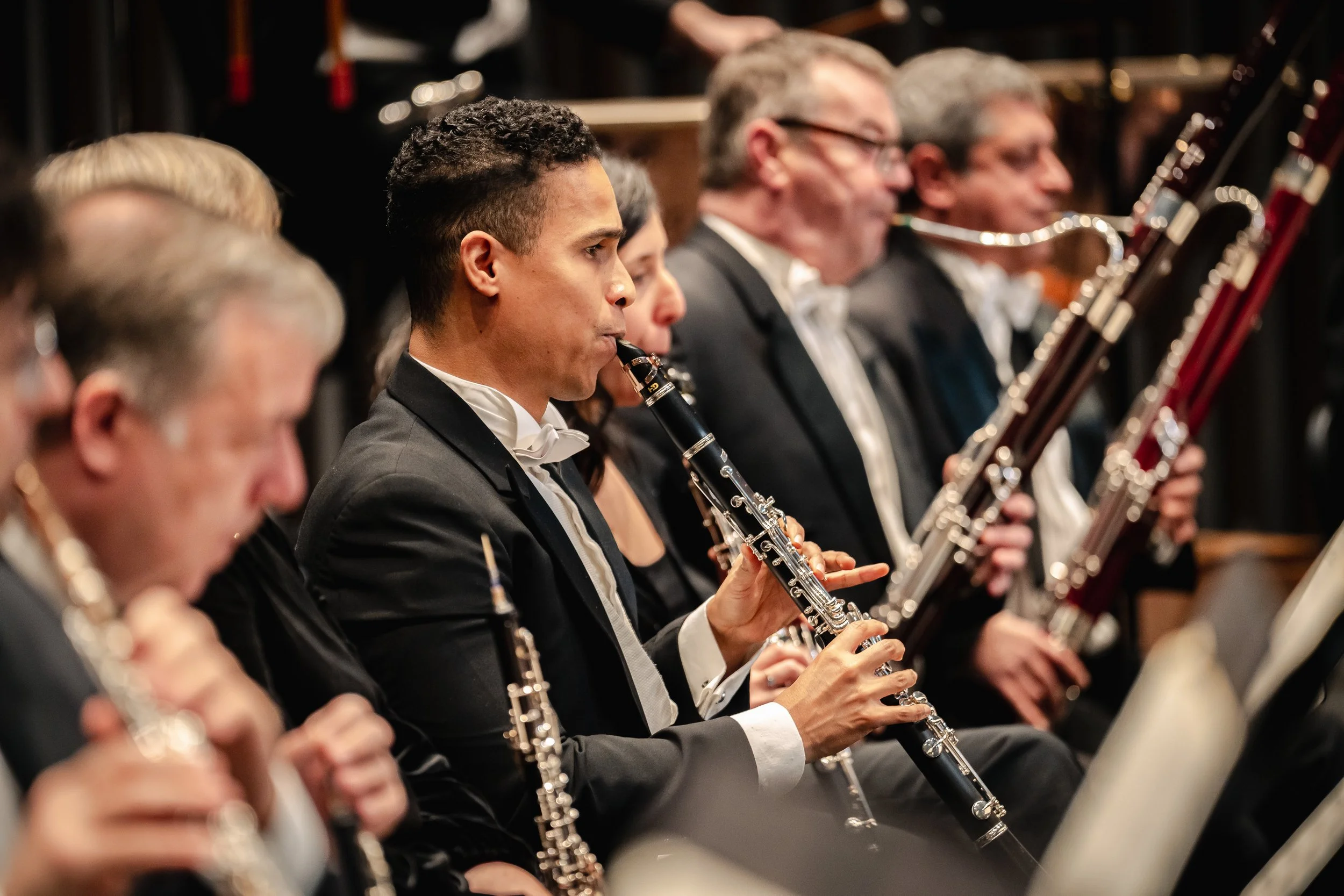 Muzikanten in formele kleding die orkestleden spelen houtblaasinstrumenten, inclusief klarinetten en fagotten, tijdens een symfonieconcert.