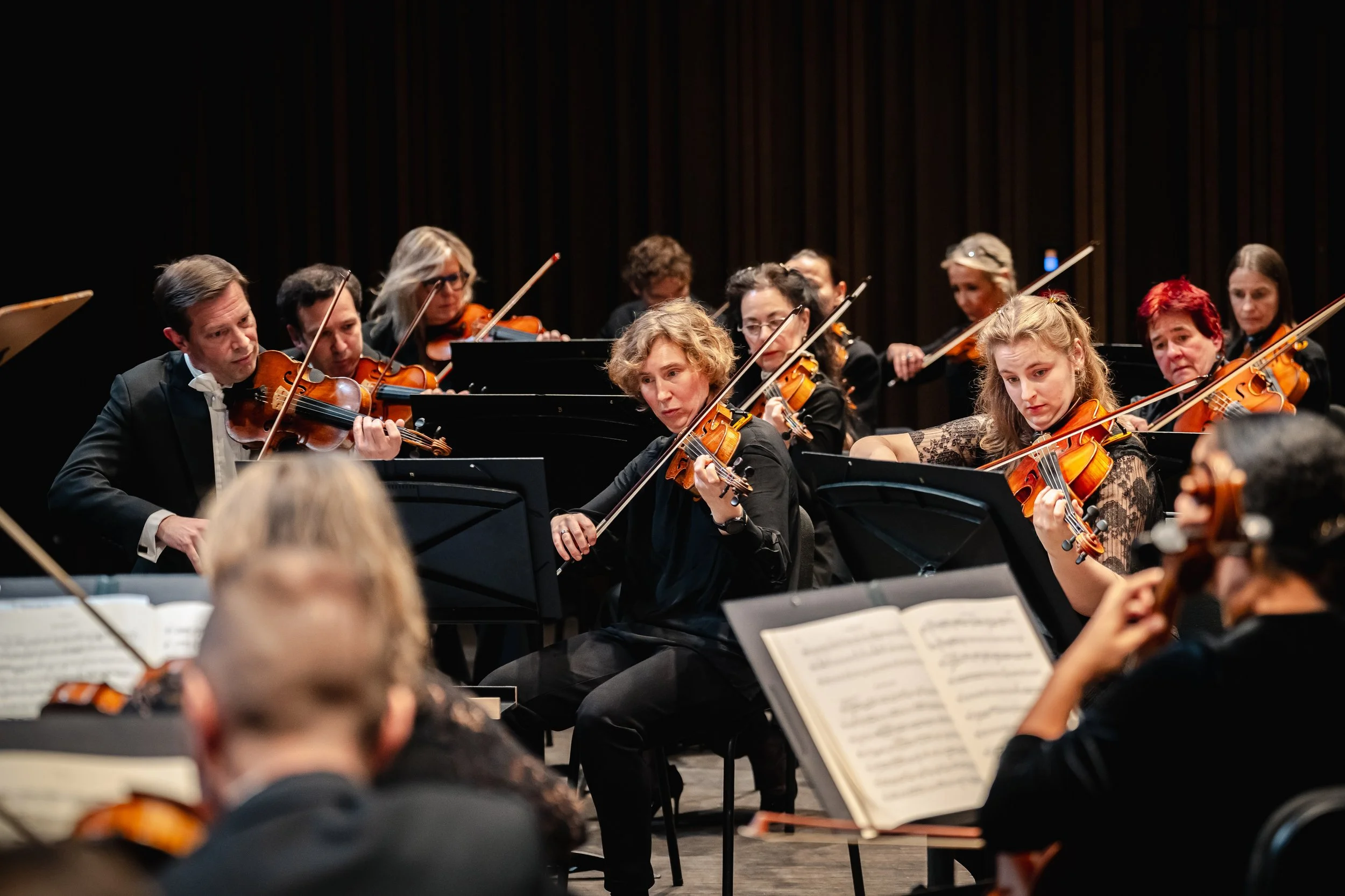 Een symfonieorkest met muzikanten die viool spelen tijdens een uitvoering op een podium.