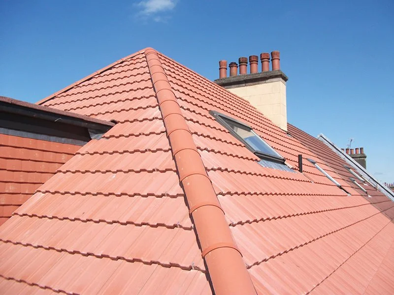 Close-up of a red tiled house roof with a chimney, skylight window, and a ladder.