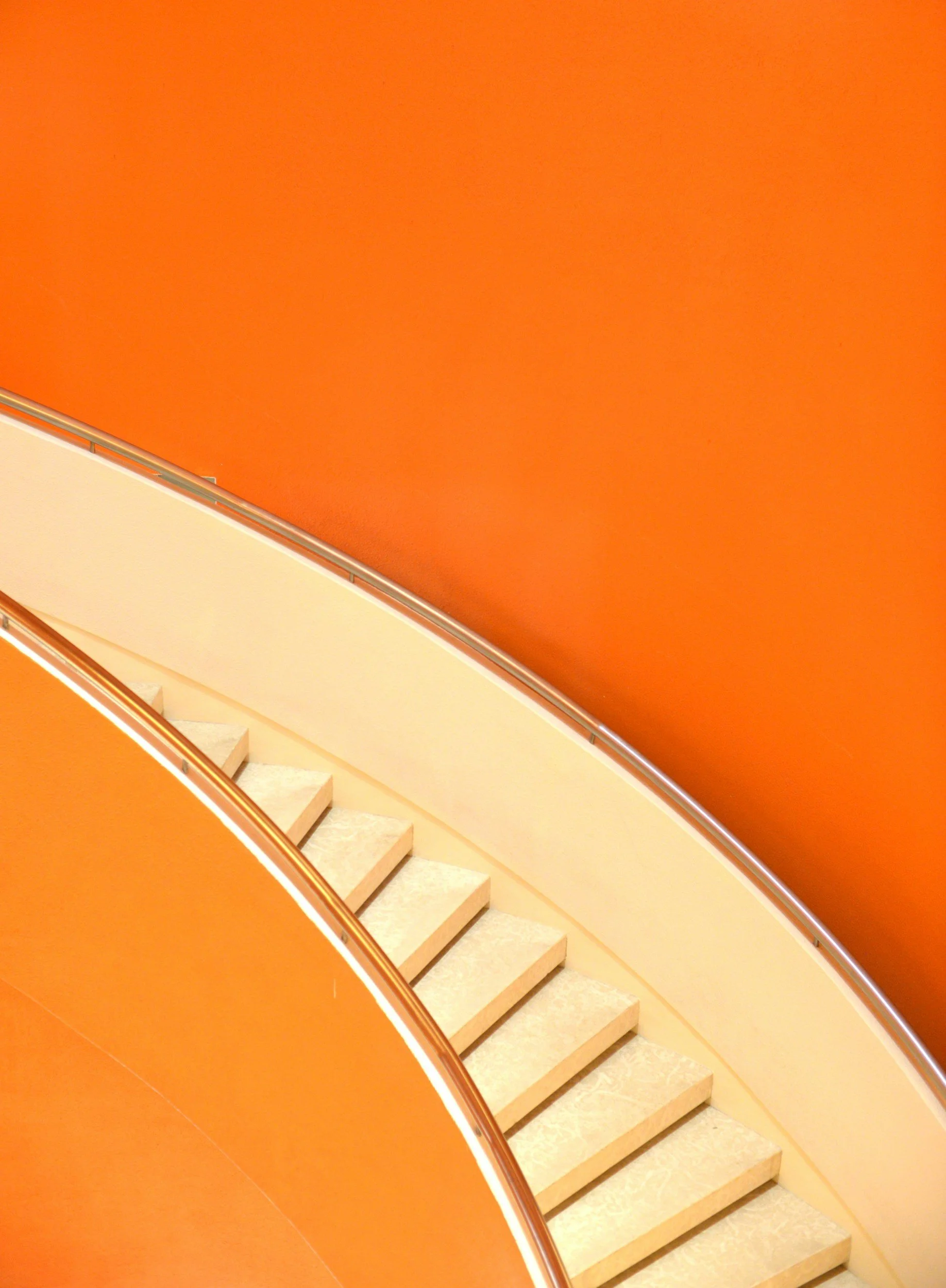 A staircase with cream-colored steps and a metal handrail set against an orange wall.