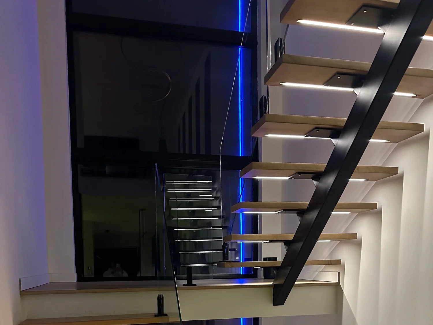 Steel central stringer staircase with floating oak treads, LED step lighting and glass railing in an Île-Perrot home