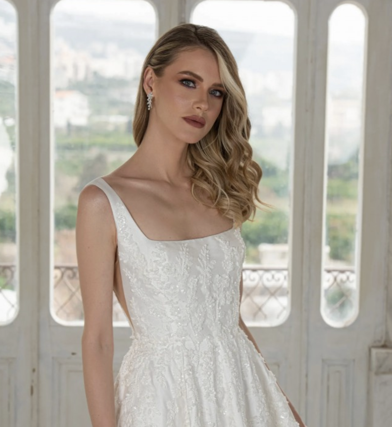This A-line is made of soft mikado fabric. The scoop neckline is modern and chic. It has dainty straps and side illusion cut-outs. It has unique beaded lace