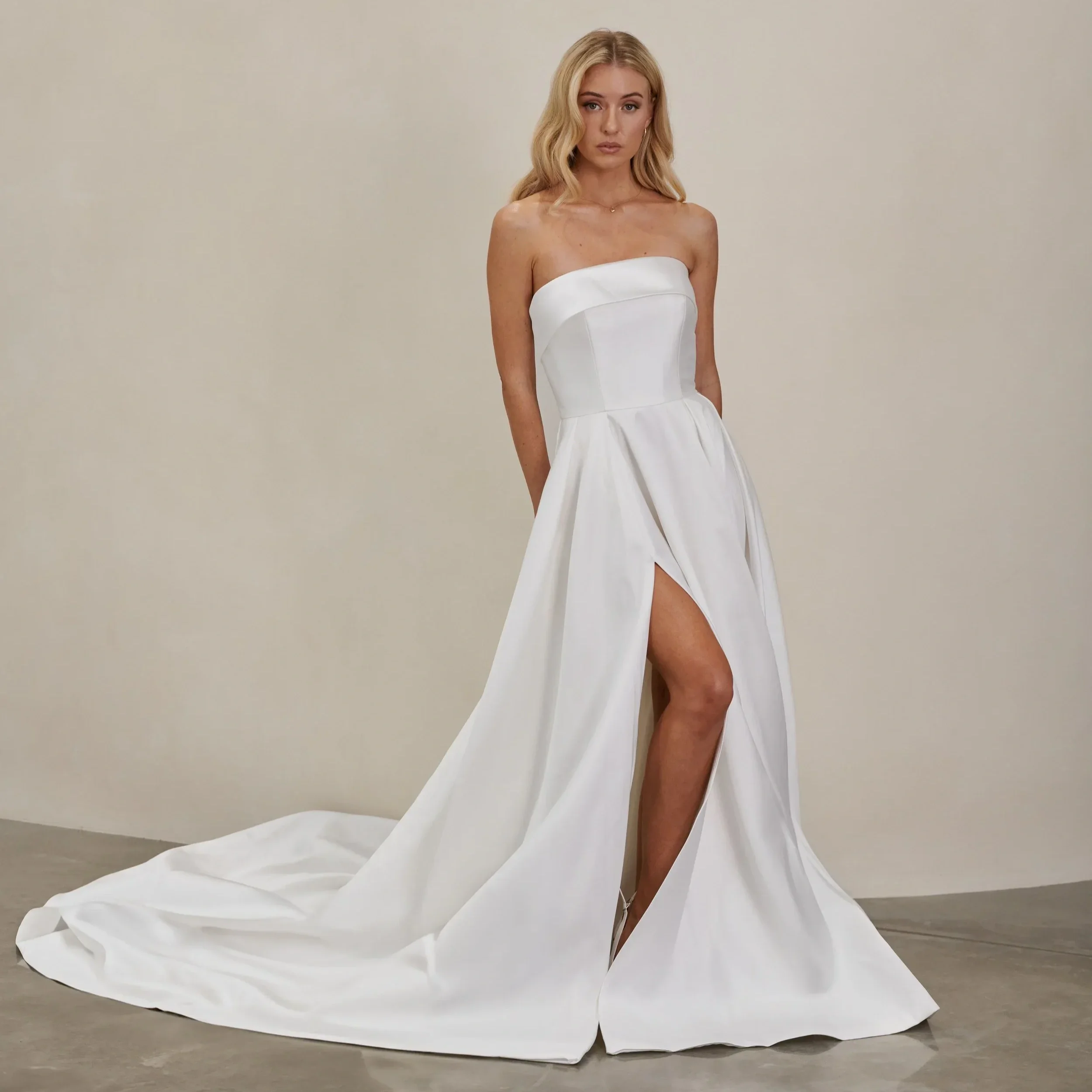 Modern satin A-line wedding gown with a strapless neckline, sleek fitted bodice, and dramatic thigh-high slit, designed for a contemporary minimalist bride.
