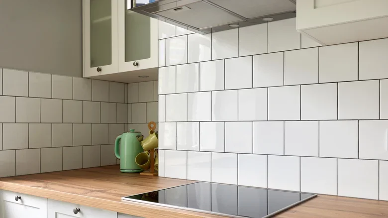 Kitchen with white tiled walls, wooden countertop, green teapot, and induction cooktop.