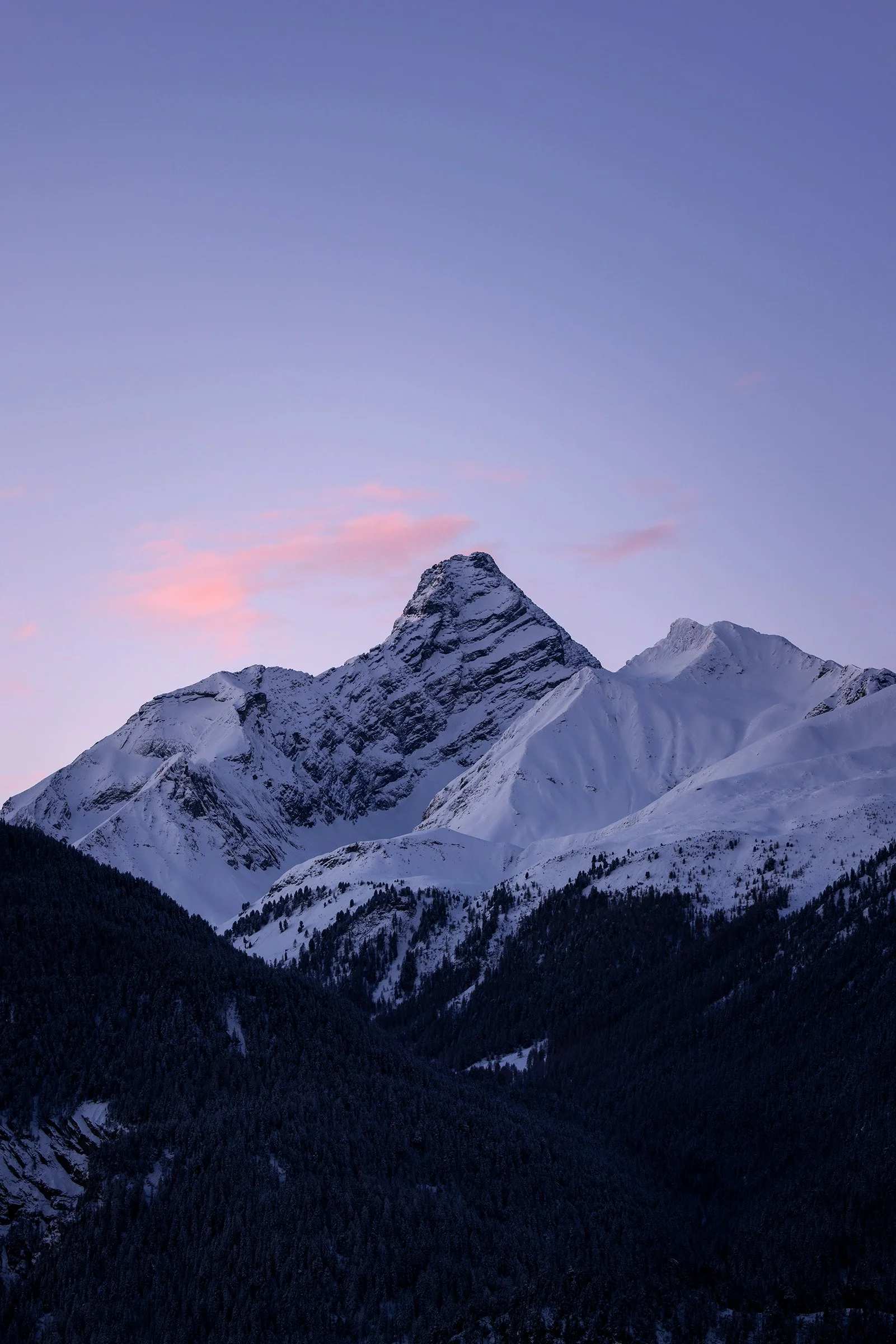 Schneebedeckte Berggipfel bei Sonnenuntergang mit Pastellfarben im Himmel.