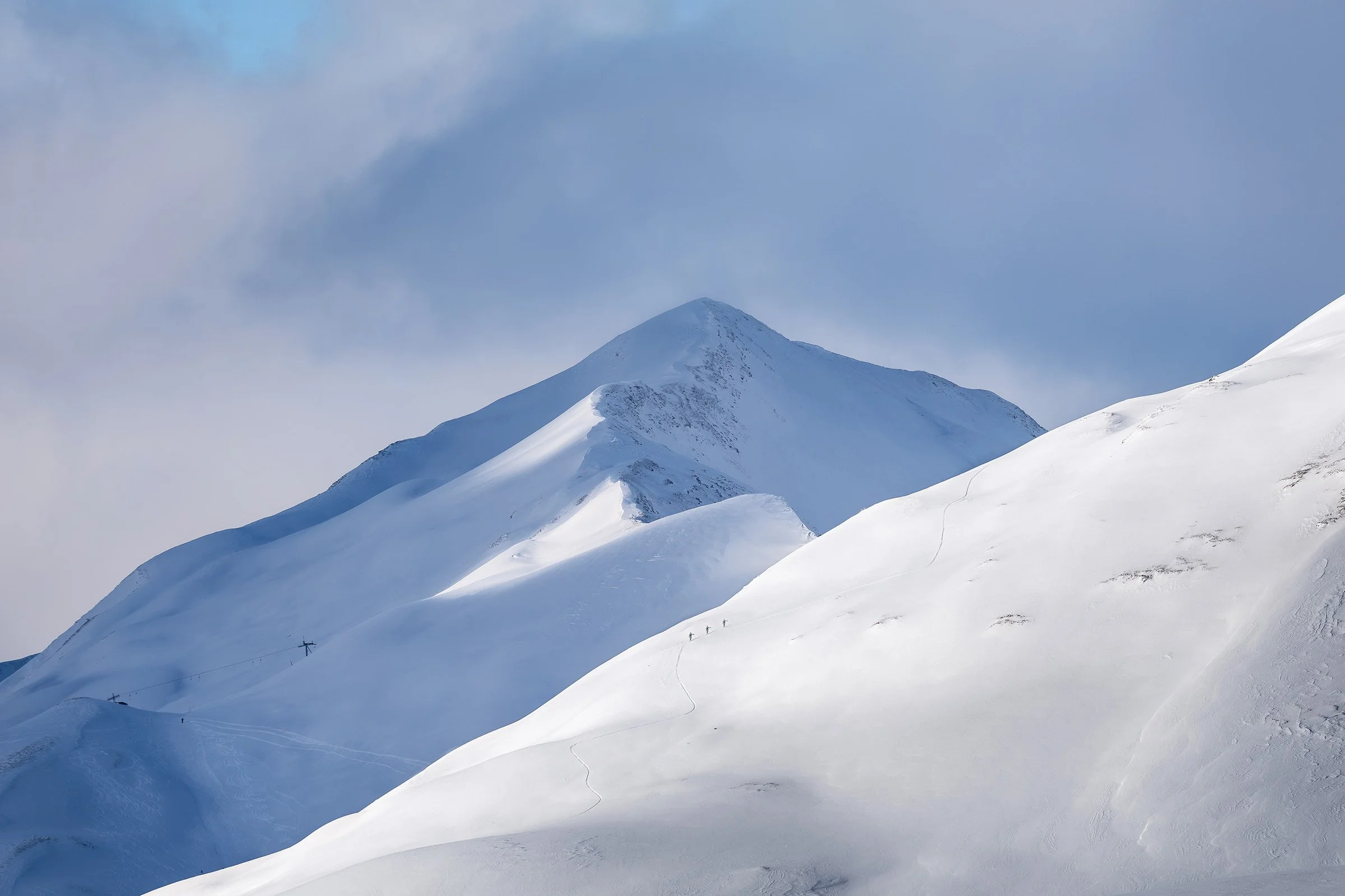 Schneebedeckte Berge unter blauem Himmel mit Sicht auf eine Skipiste und Skilift.
