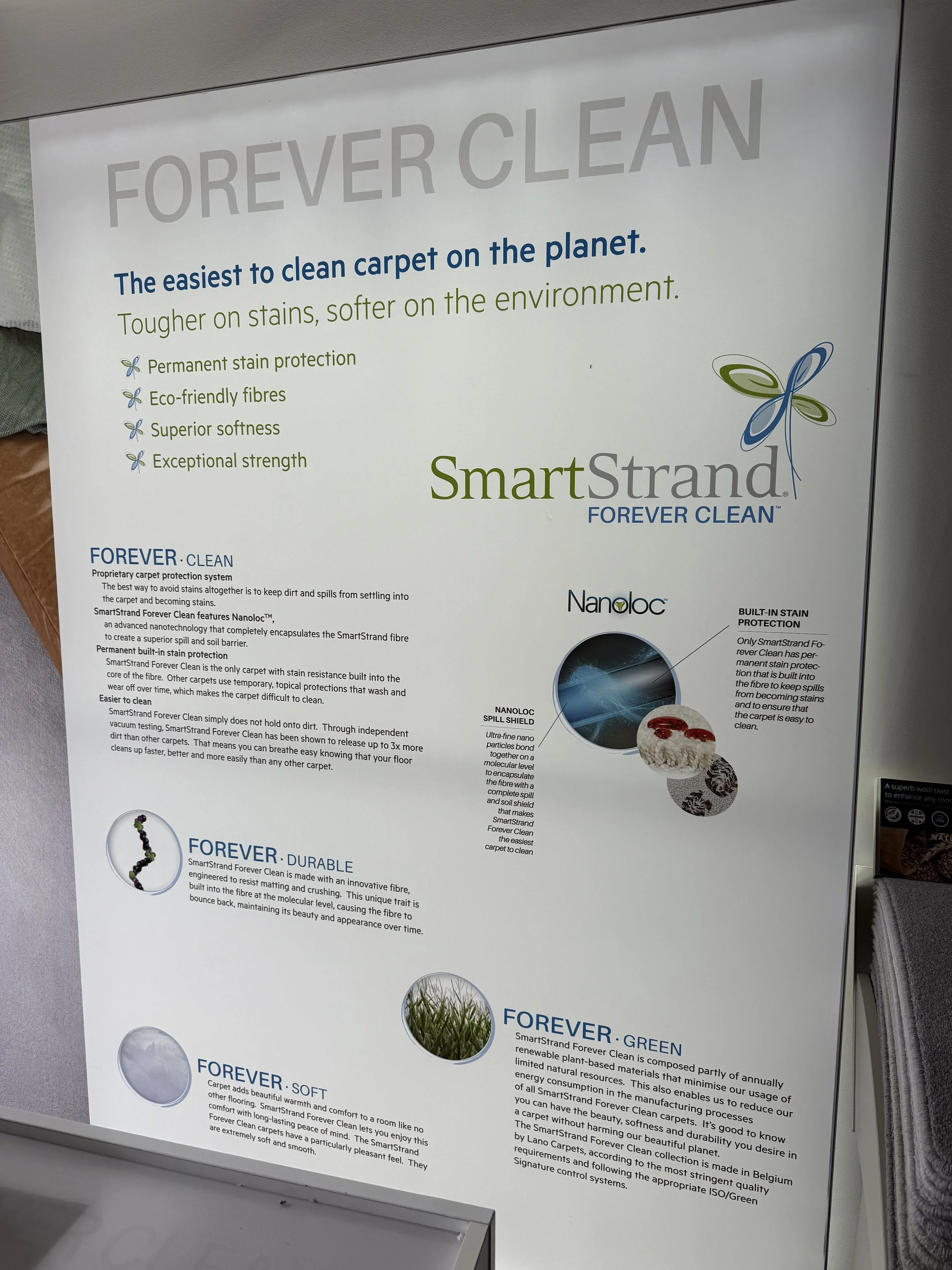 An informational sign about SmartStrand Forever Clean carpet, highlighting its features like stain protection, eco-friendly fibers, softness, durability, and environmental benefits.