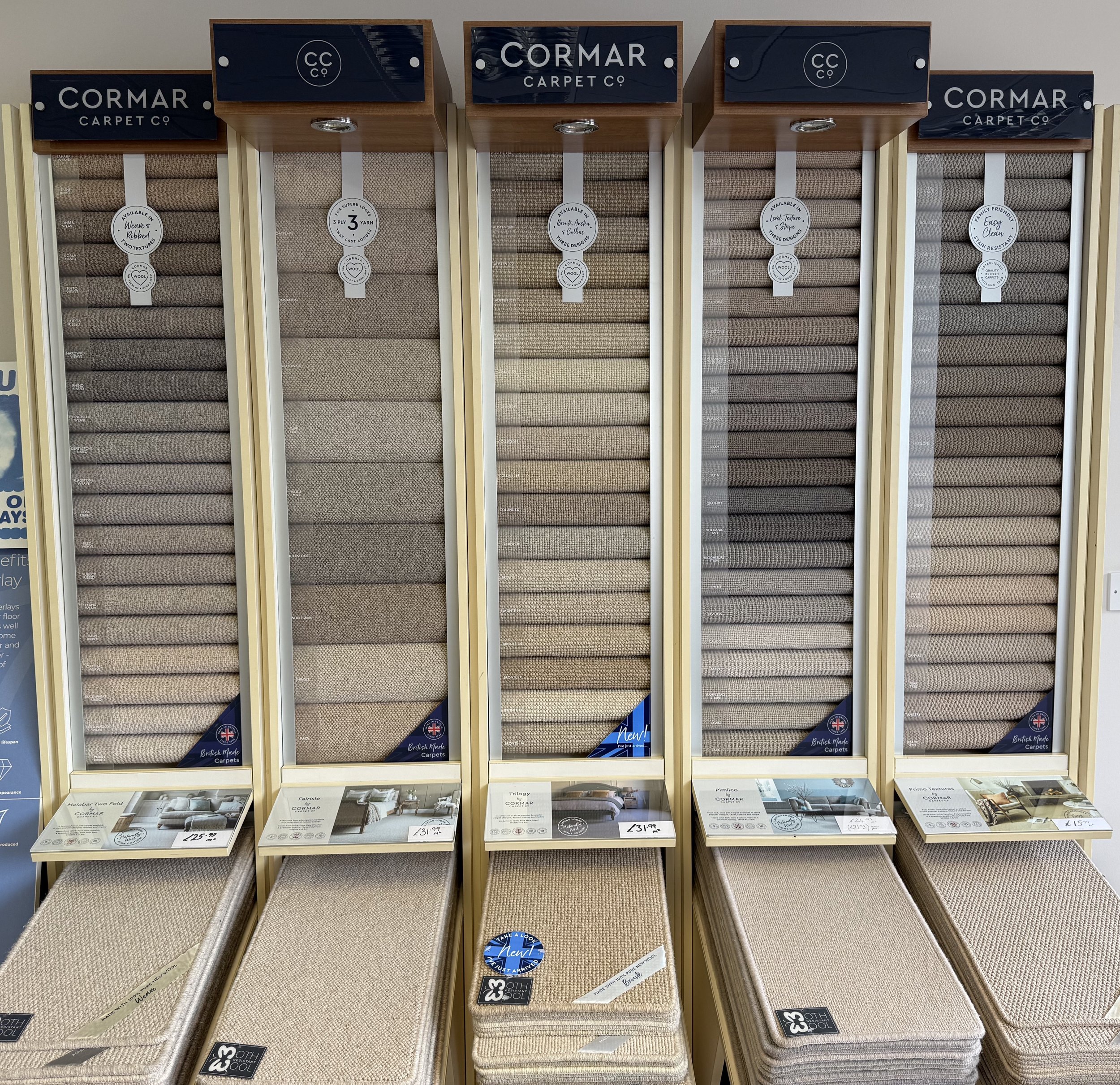 Display of carpet samples in a store, labeled as Cormar Carpet Co, arranged vertically with fabric swatches and prices.