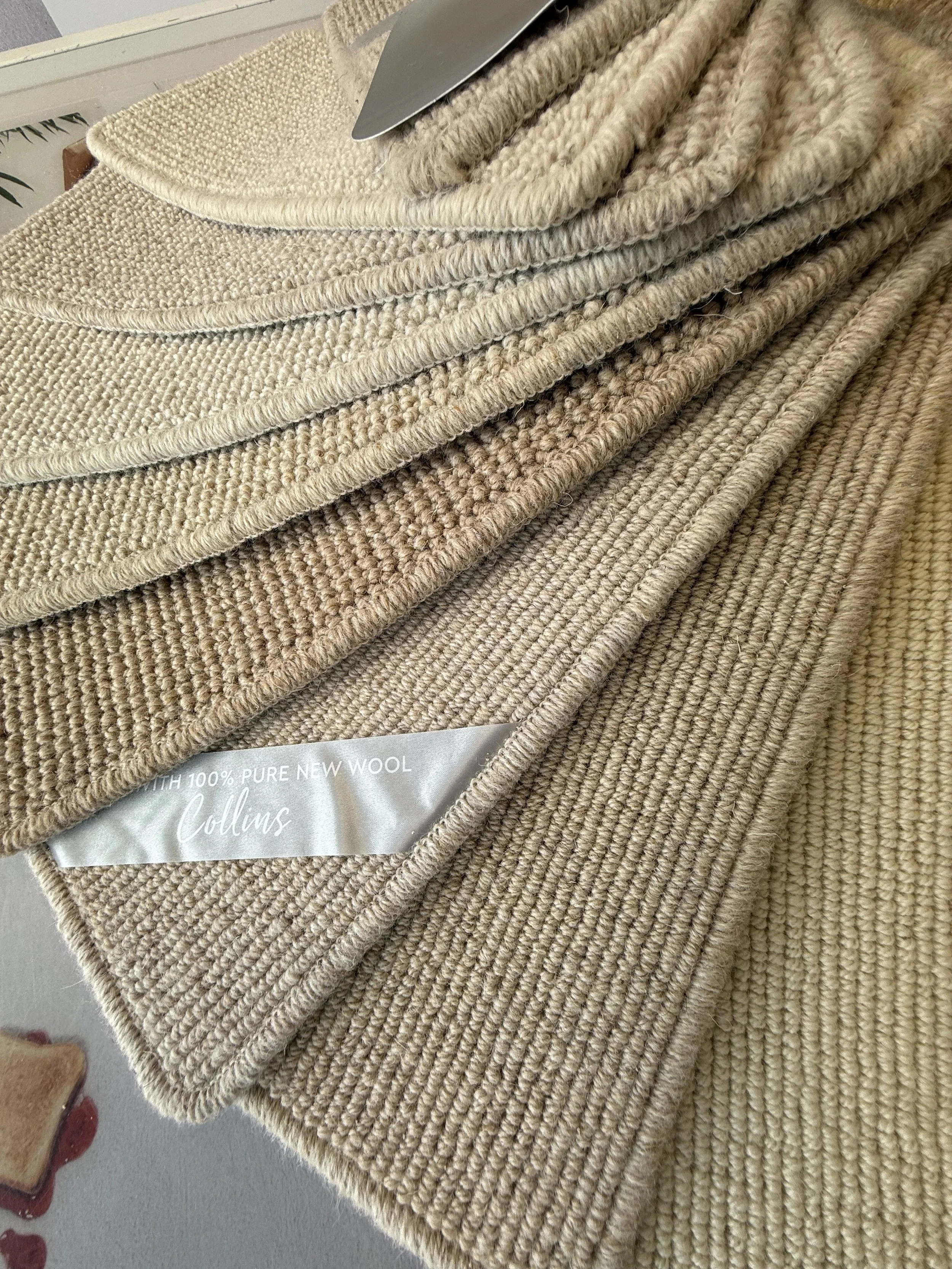 Cormar Carpet - Stacked beige and light brown wool sweaters with a tag that reads '100% Pure New Wool' and 'Collins'.
