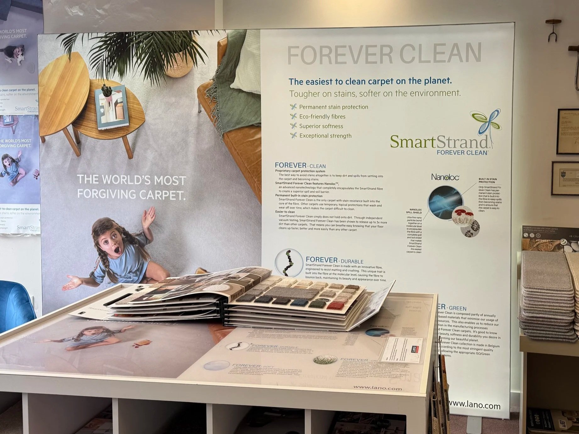 Display board advertising SmartStrand Forever Clean Carpet with information on its stain protection, eco-friendliness, softness, and strength, with an image of a woman on a grey carpeted room, and a toddler on the carpet looking surprised.