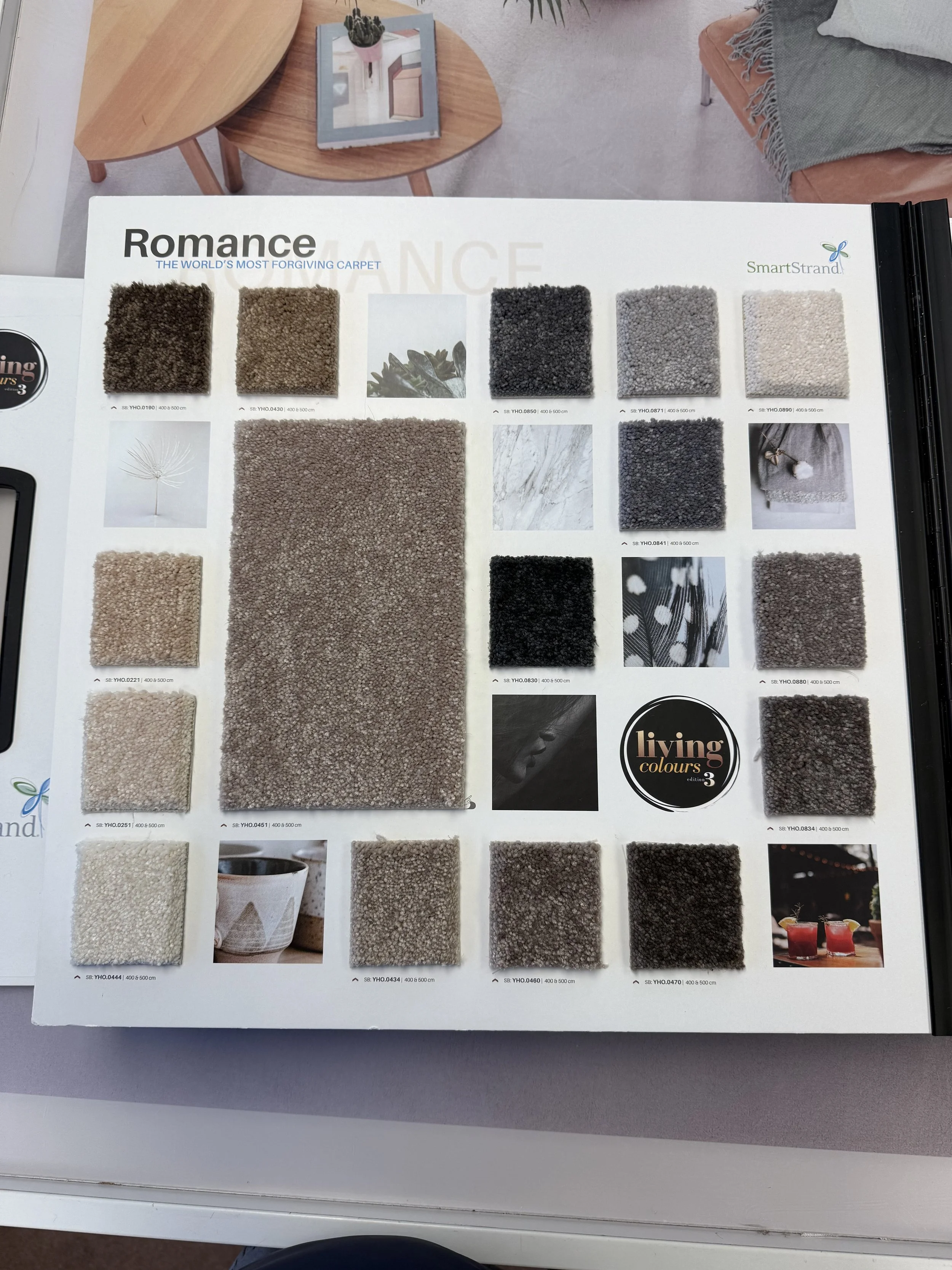 A Smartstrand carpet sample catalog titled "Romance" with various swatches of beige, gray, black, and cream carpets, along with some decorative photos and a "living colours" logo.