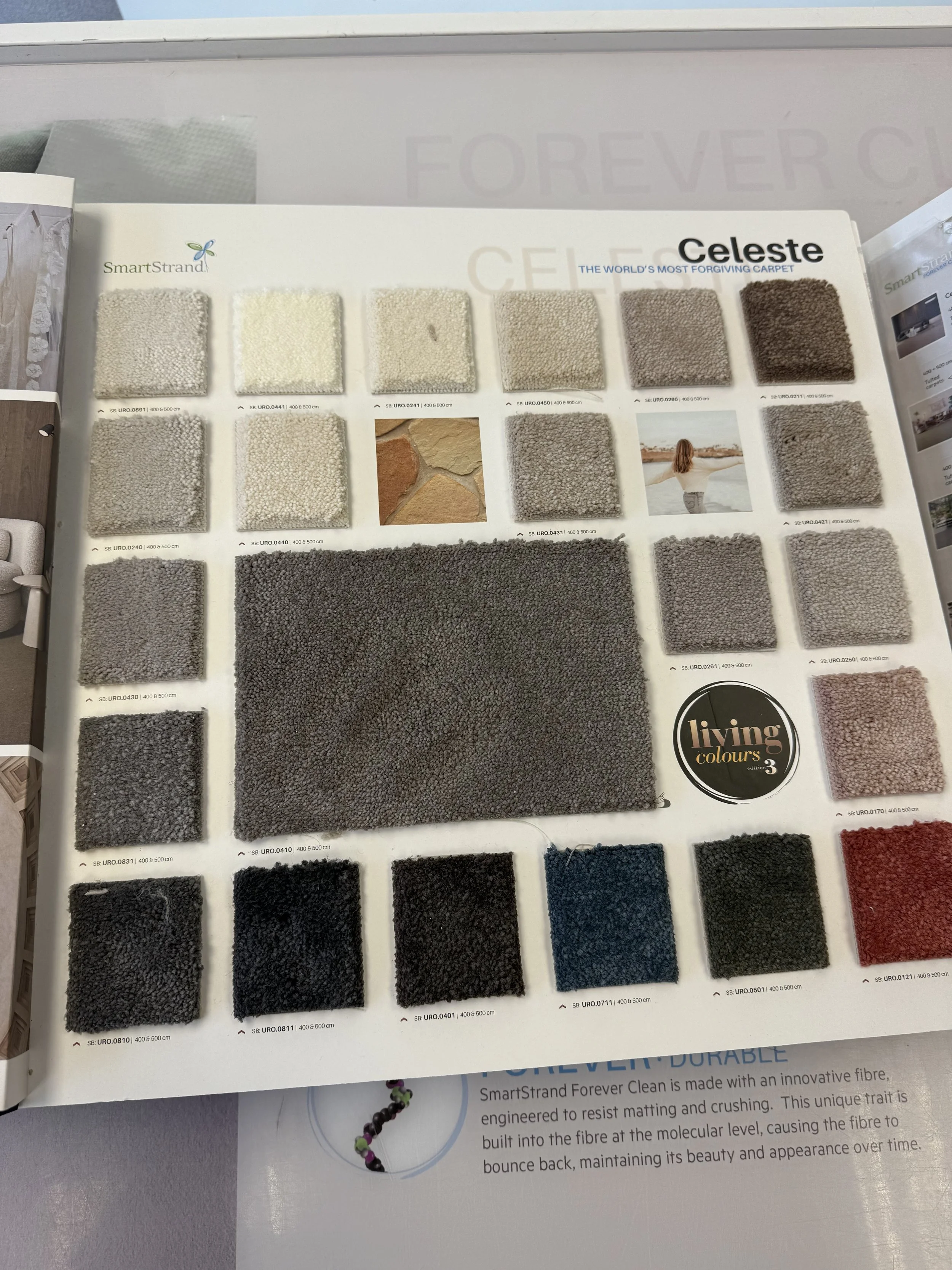 A Smartstrand carpet sample display board with various shades of neutral and dark colored carpets, some with textured patterns and a small picture of a woman on the right side.