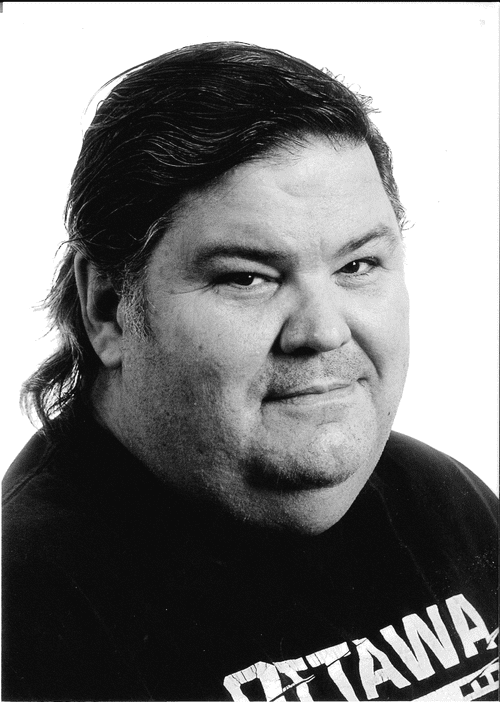 David Gabriel - Black and white portrait of a man with dark hair, side-swept, wearing a black shirt smiling slightly.