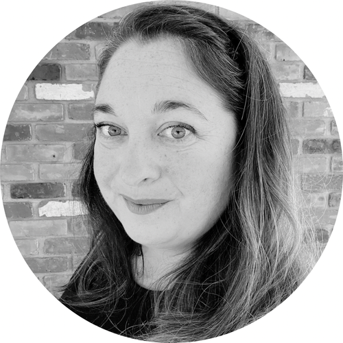 Anne Payette - A woman with long wavy hair and light eyes, smiling slightly, in front of a brick wall.