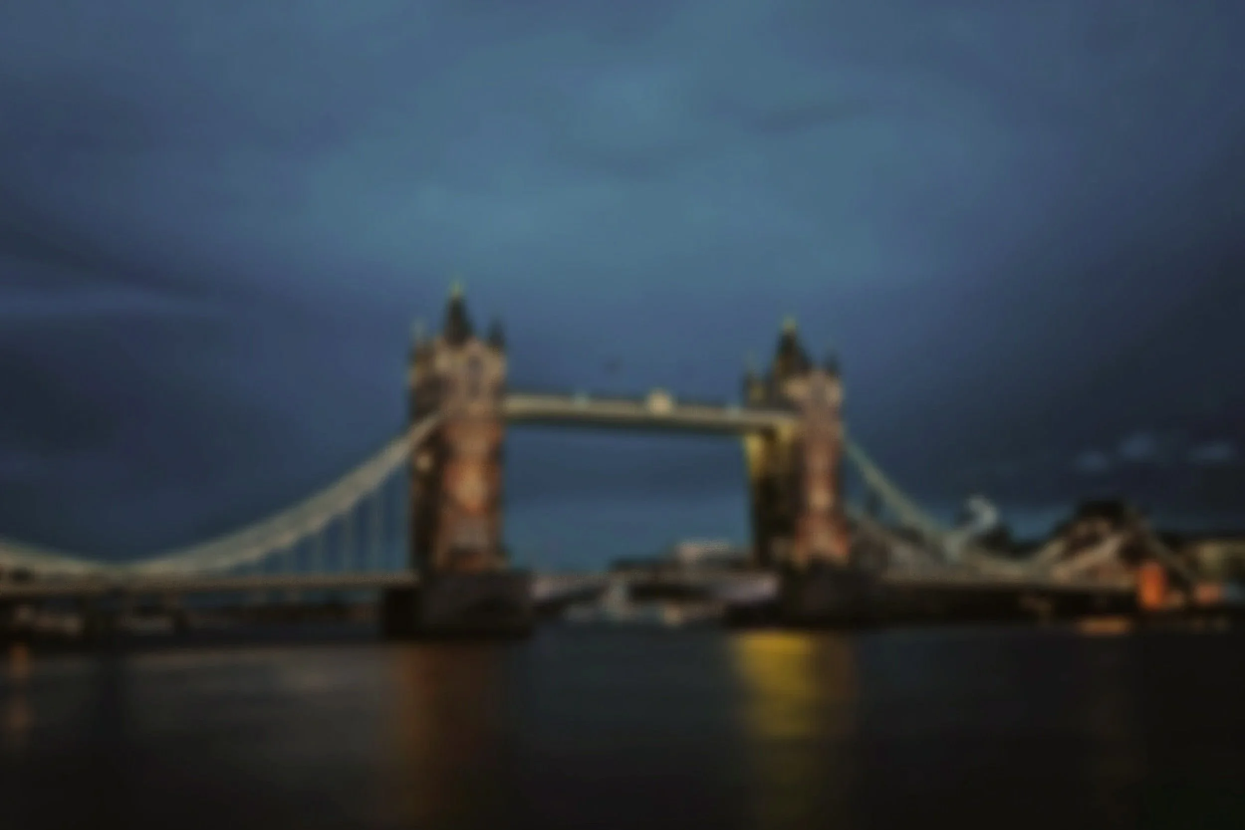 Blurred night view of Tower Bridge in London with cloudy sky and reflections on the river.