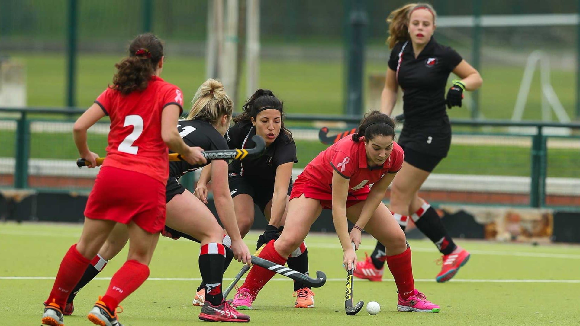 Female field hockey players competing for control of the ball on a green turf field.