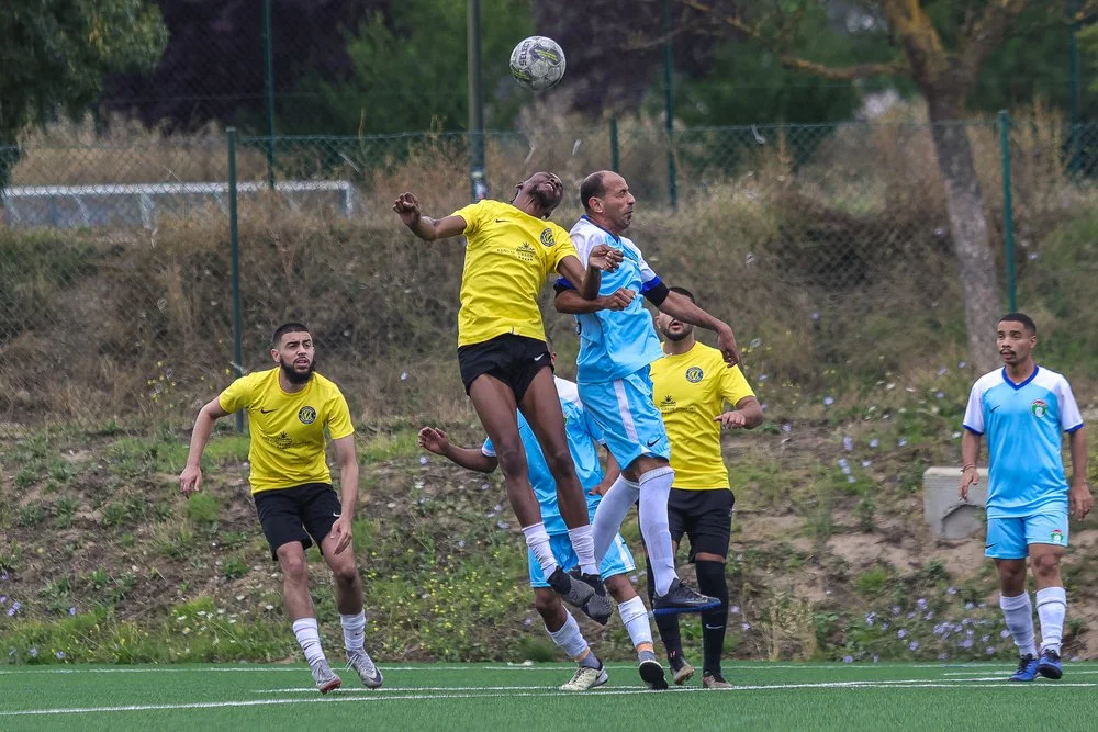 Soccer players in yellow and blue jerseys jumping and heading the ball during a match on a grassy field.