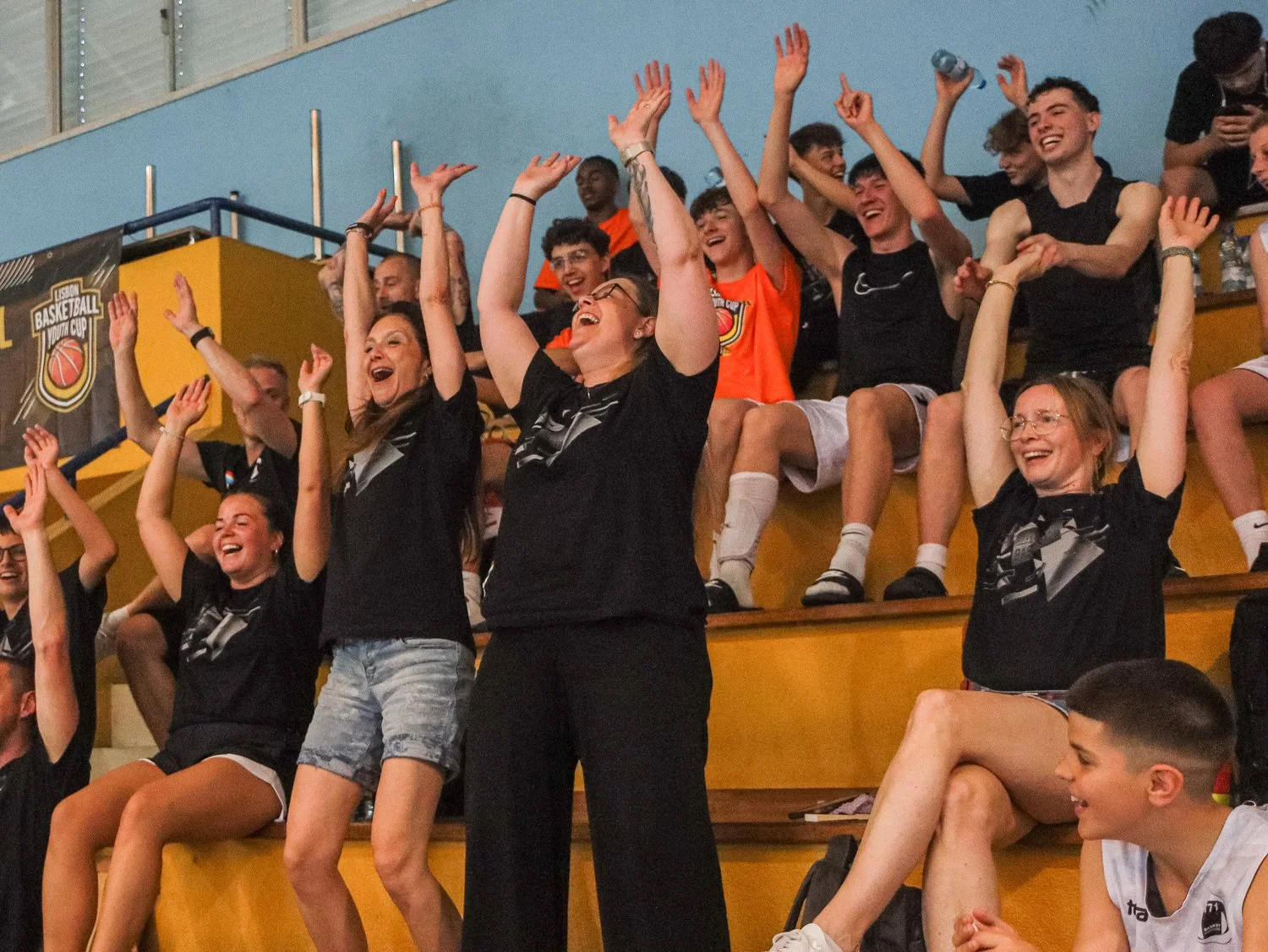 Spectators celebrating in the stands during a match at the Lisbon Basketball Youth Cup indoor arena.