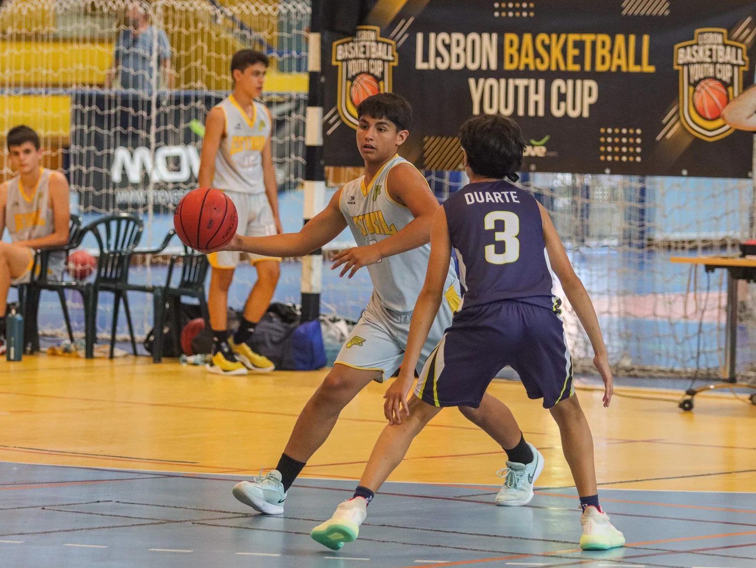Boys playing an indoor basketball game at the Lisbon Basketball Youth Cup, with tournament branding visible in the background.