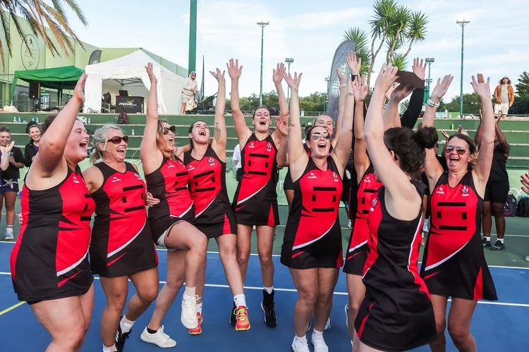A women's netball team in red and black uniforms celebrating.jpg