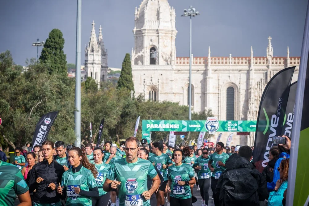 Participants running through the streets of Lisbon during the Bimbo Global Race, with a historic city landmark in the background.