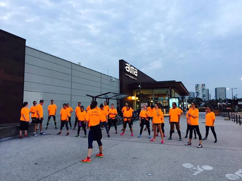 Group of people in orange shirts gathered outside a building with the sign 'alma' during dusk.