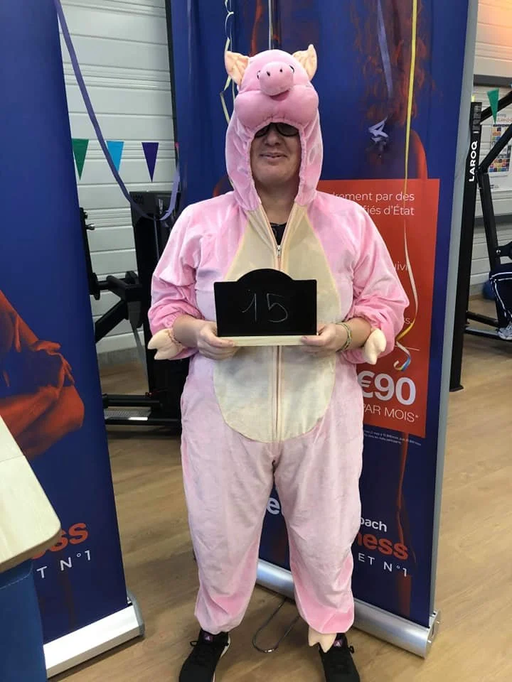 Person dressed in a pink pig costume holding a blackboard with the number 15.