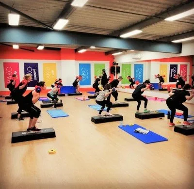 Group exercise class in a fitness studio with participants using step platforms for a workout.