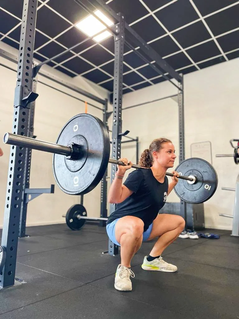 Man smiling and exercising on a fitness machine at a gym, with a woman working out in the background.