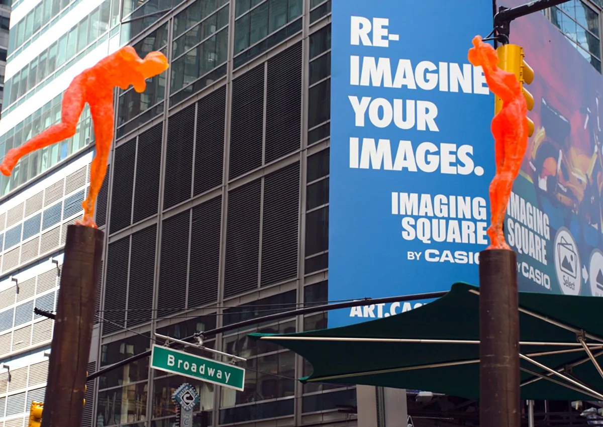 Two glowing orange street art sculptures on top of black poles in an urban setting. Large blue billboard with white text reading 'Re-imagine Your Images,' and the street sign 'Broadway' visible below.