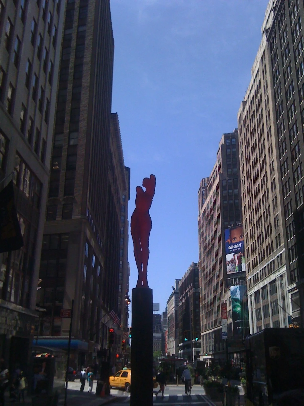 Tall buildings line the street in New York City with a red sculpture of a woman for the I Love NY campaign in the center.