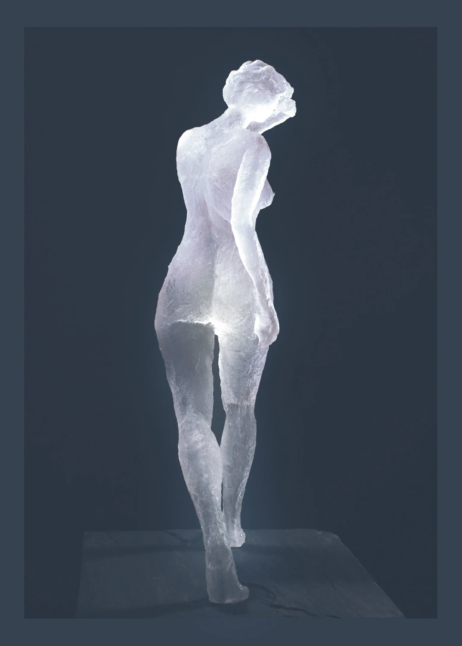 Icicle clear sculpture of a woman with short hair, standing on a snowy surface, illuminated against a dark background.